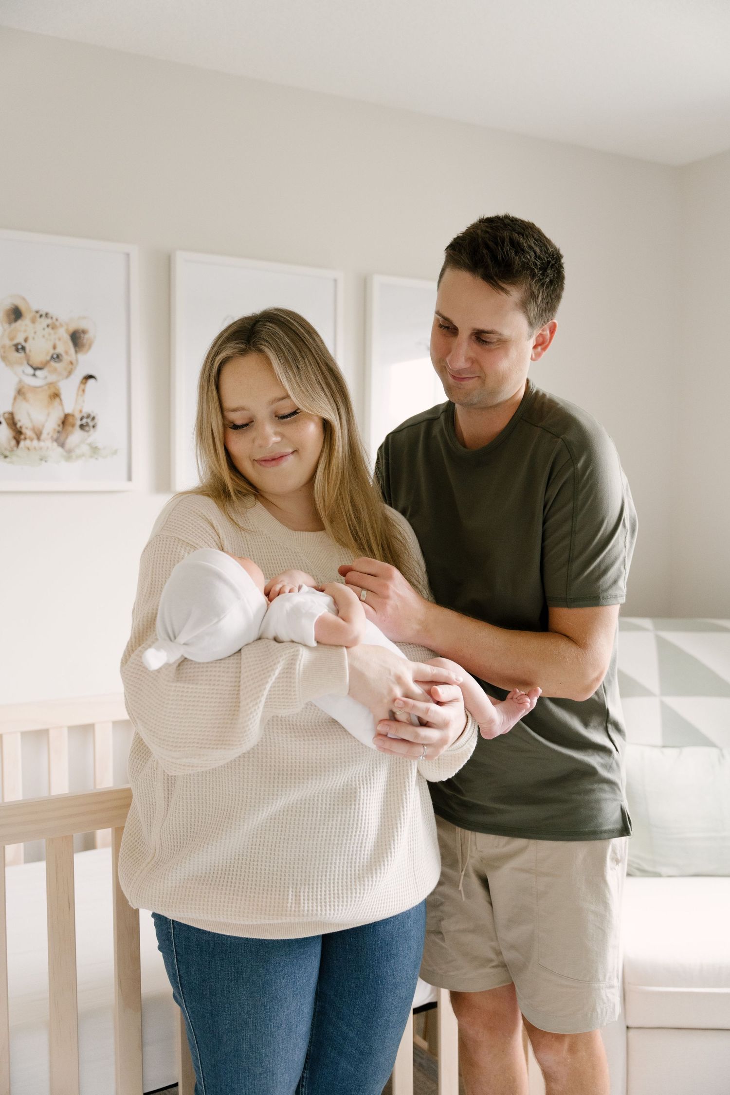 Smiling couple standing by crib in nursery holding and admiring their newborn baby together.