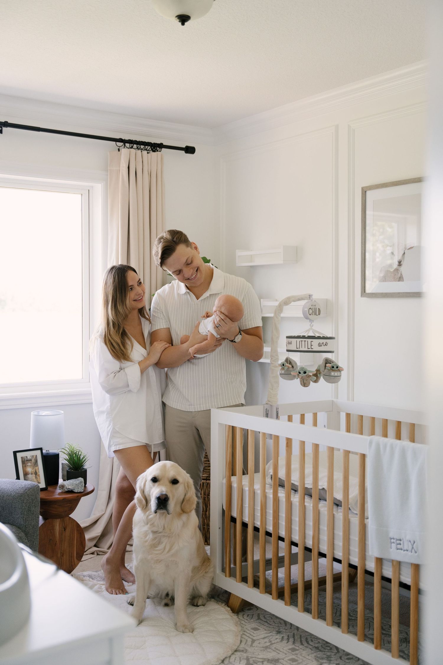 Happy parents with golden retriever dog standing beside baby crib in nursery.