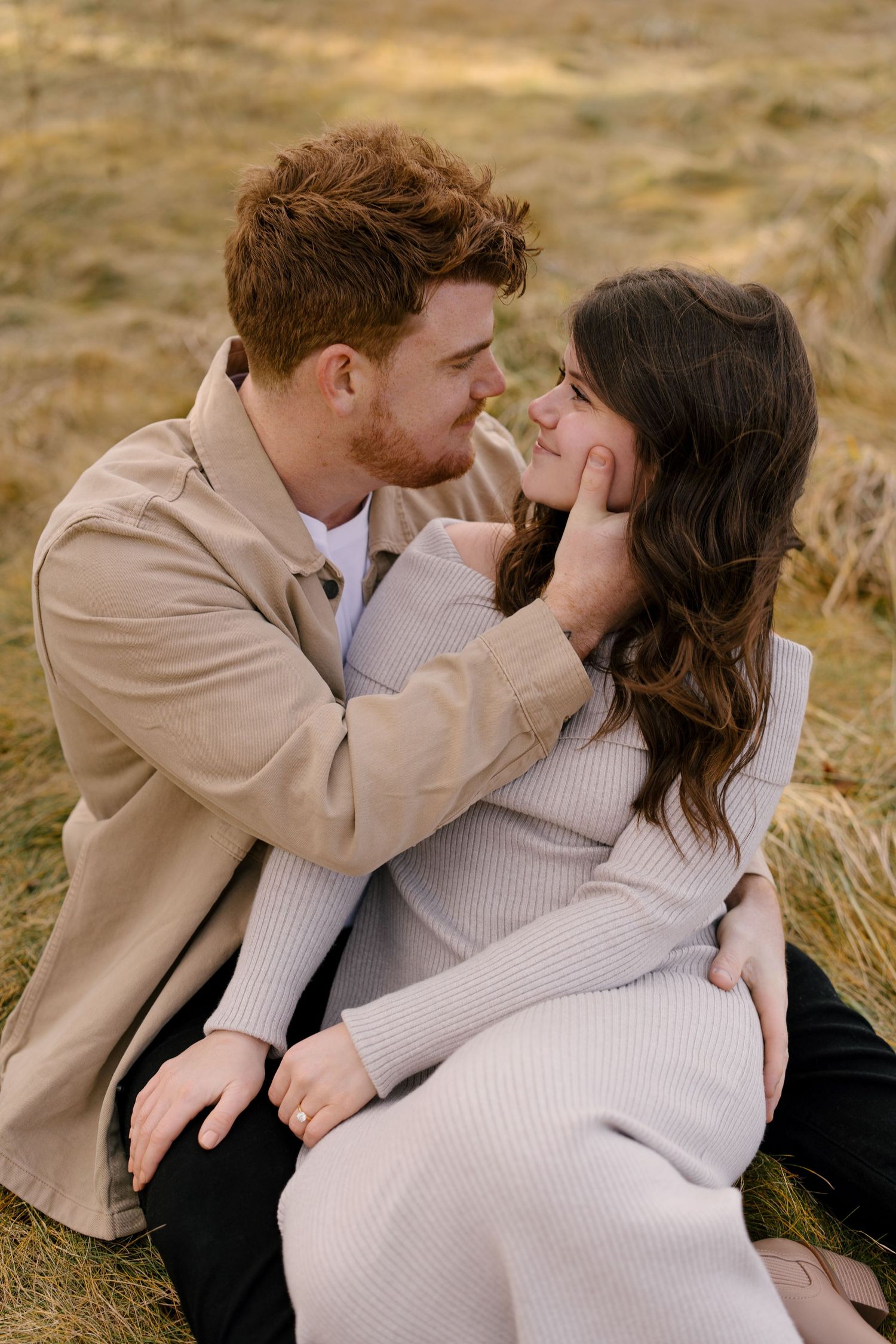 Romantic couple sitting in a golden field, man gently cupping womans face as they lean in.