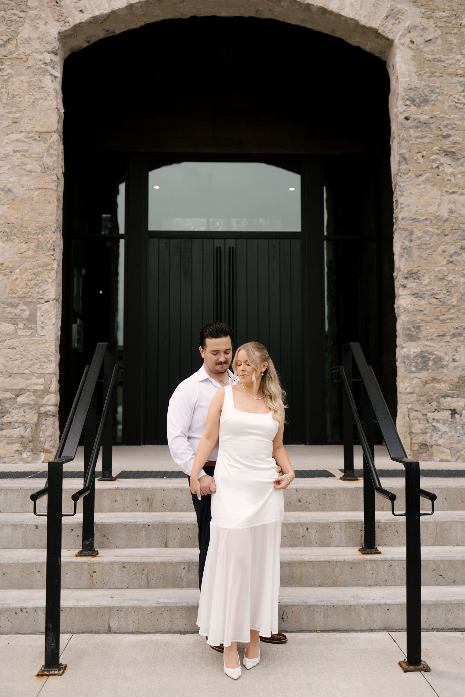 Couple posing together on stone steps outside a historic building with black arched doors.