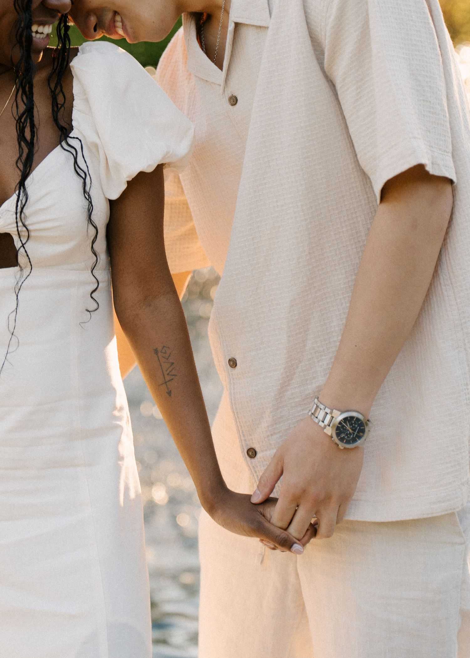 Close-up of interracial couple holding hands, man wearing silver watch, in warm golden sunlight.