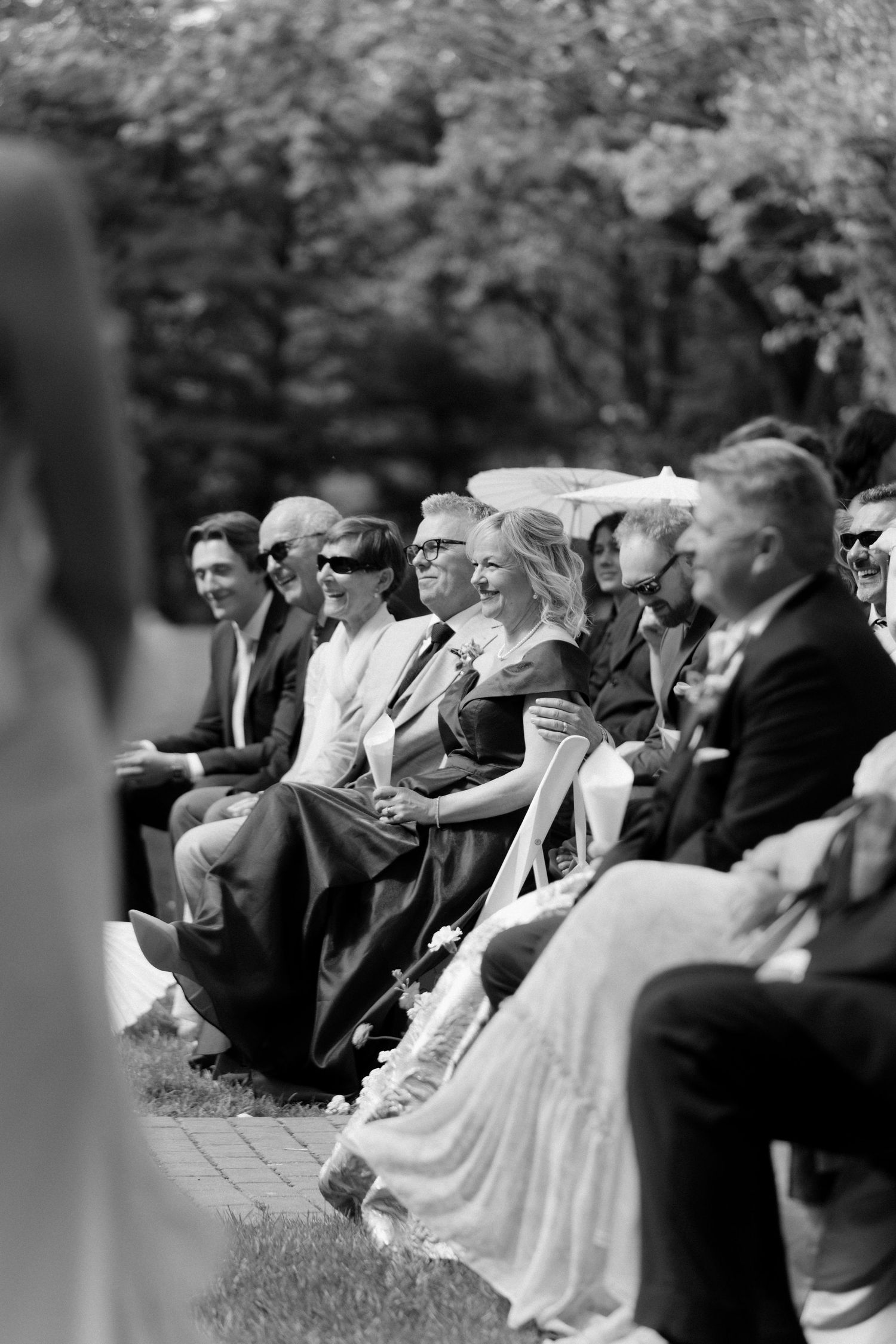 Wedding guests laugh and smile while seated at an outdoor ceremony on a sunny day at Roseville Estates wedding venue.