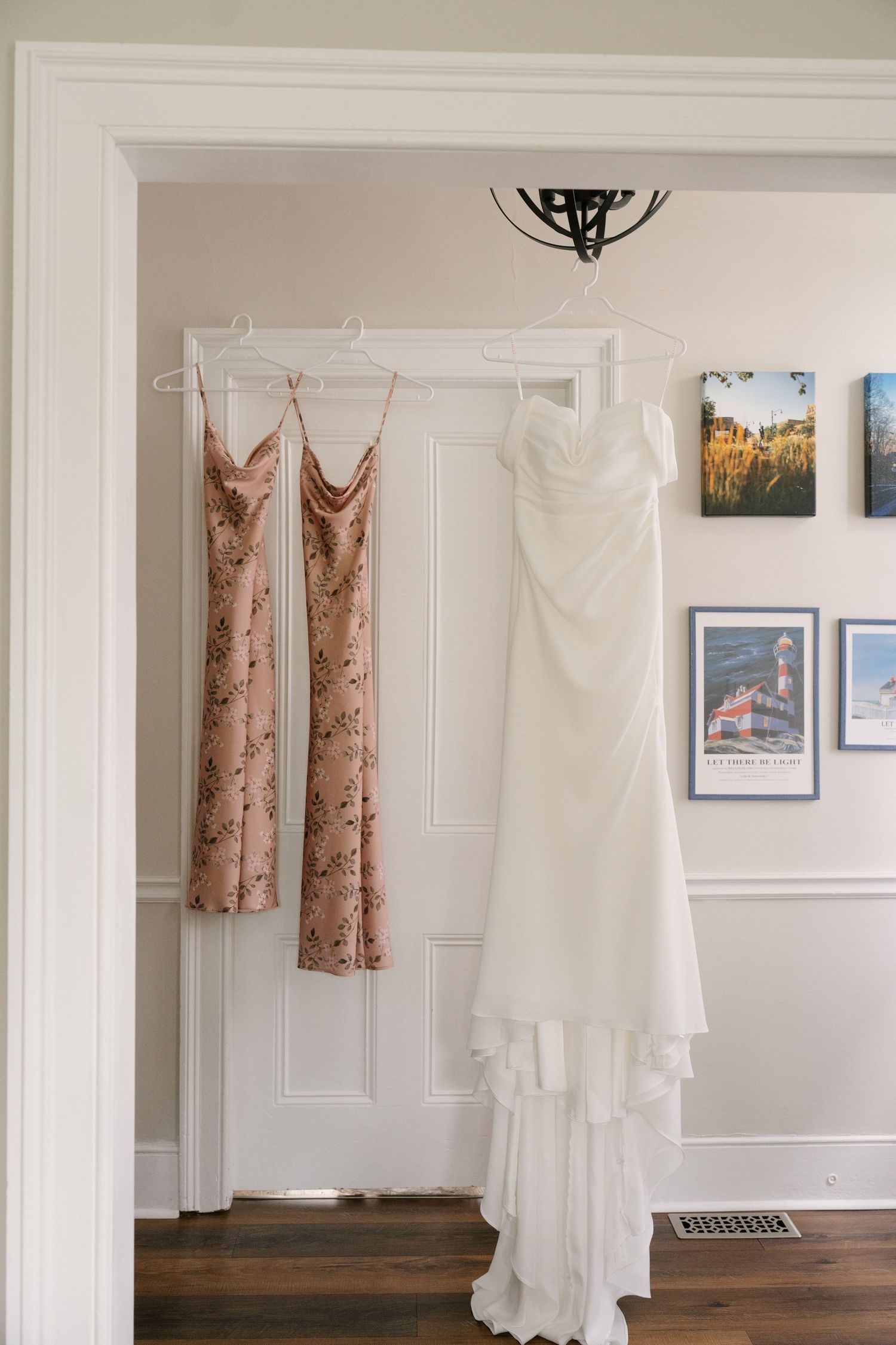 White strapless bridal gown and floral bridesmaid dress hanging on door in elegant room.