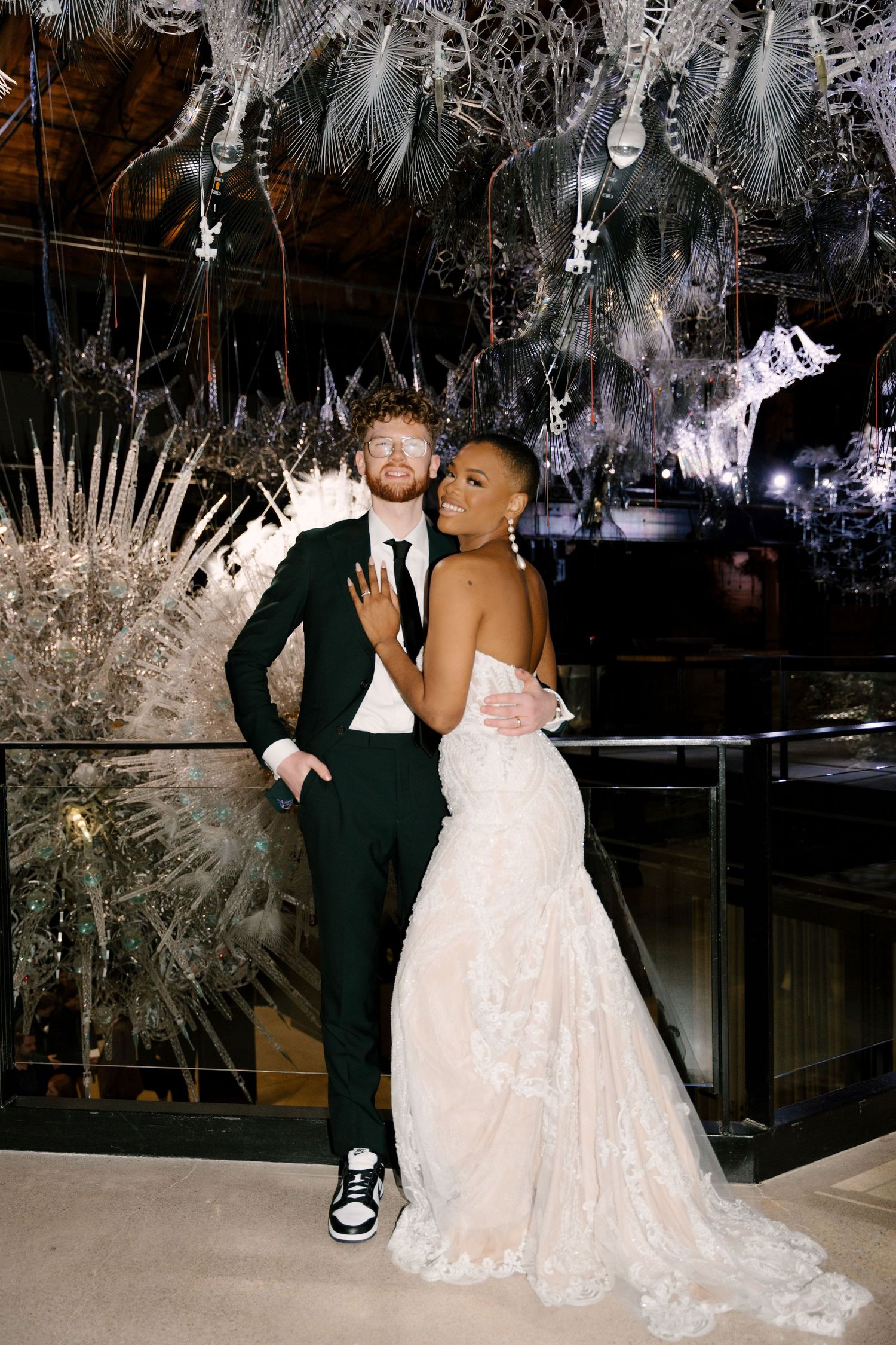 Elegant newlywed couple posing together under a dramatic crystal and floral chandelier installation at Tapestry Hall.