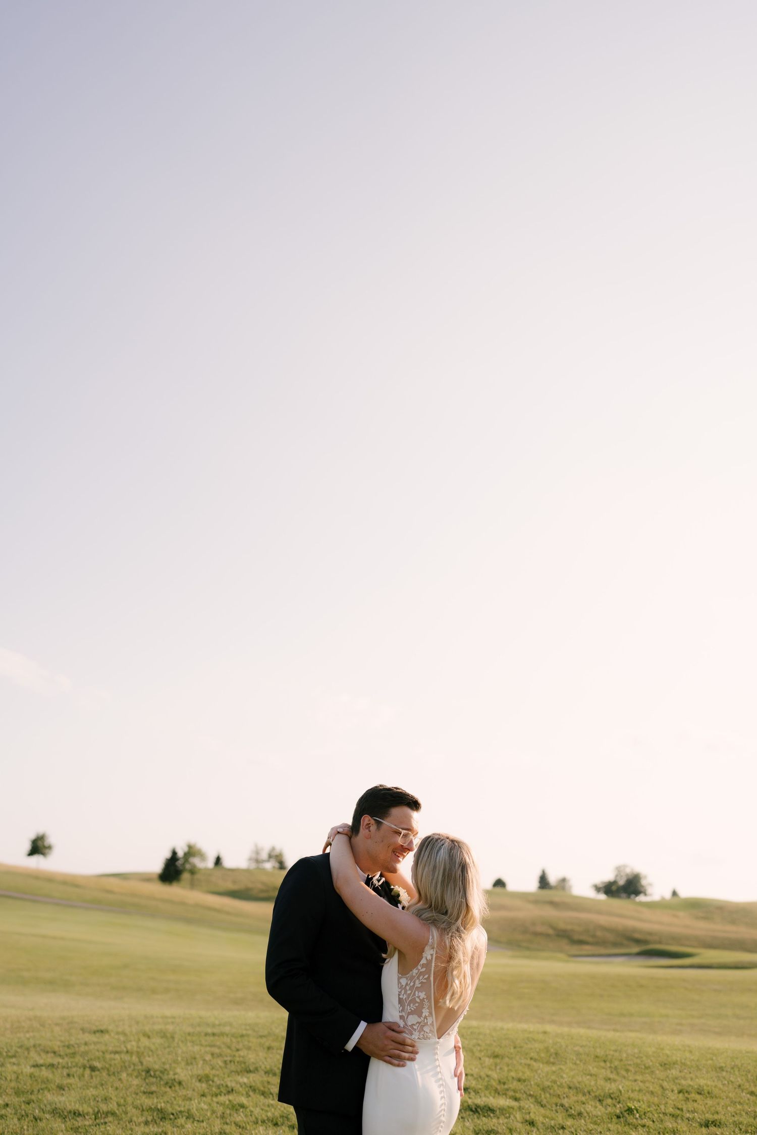 Bride and groom sharing a romantic kiss on a golf course at golden hour under a clear sky.