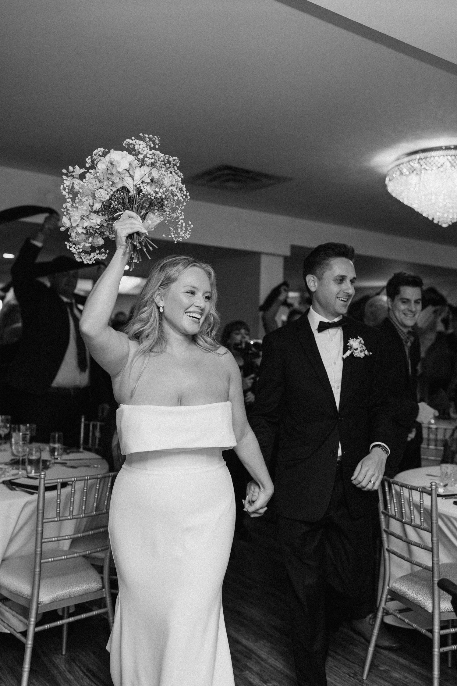 Bride and groom making grand reception entrance, bride raising bouquet, in elegant ballroom.