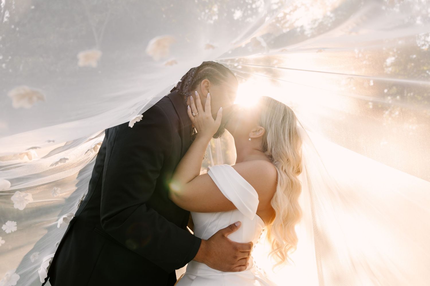 Newlyweds kiss beneath wedding veil with sun flare creating dreamy backlit effect at Whistle Bear wedding venue.