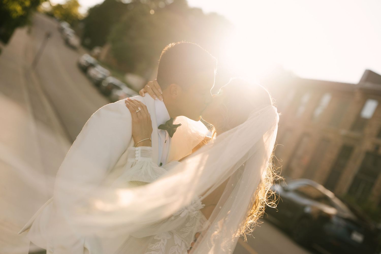 Bride and groom sharing a romantic kiss bathed in warm golden sunset light outdoors.