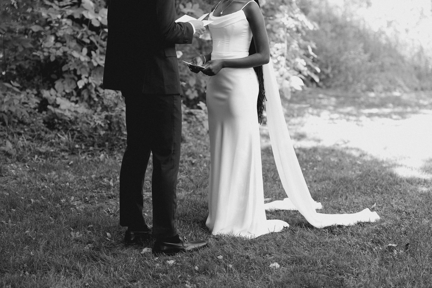 A black and white photo of a bride and groom reading their wedding vows together on a grassy lawn at Wren House.