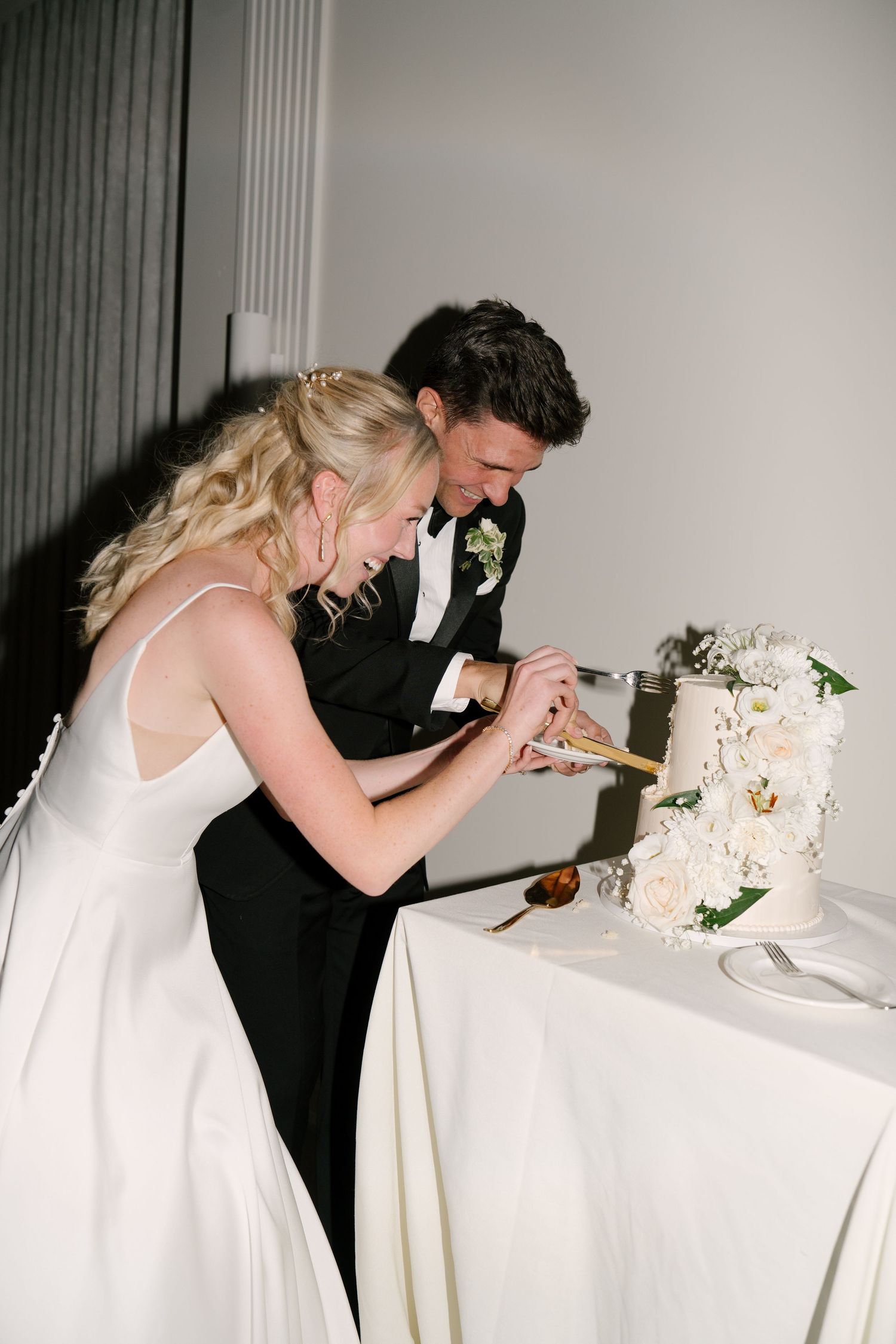 Bride and groom leaning in together to cut their elegant white wedding cake at Roseville Estates wedding venue.
