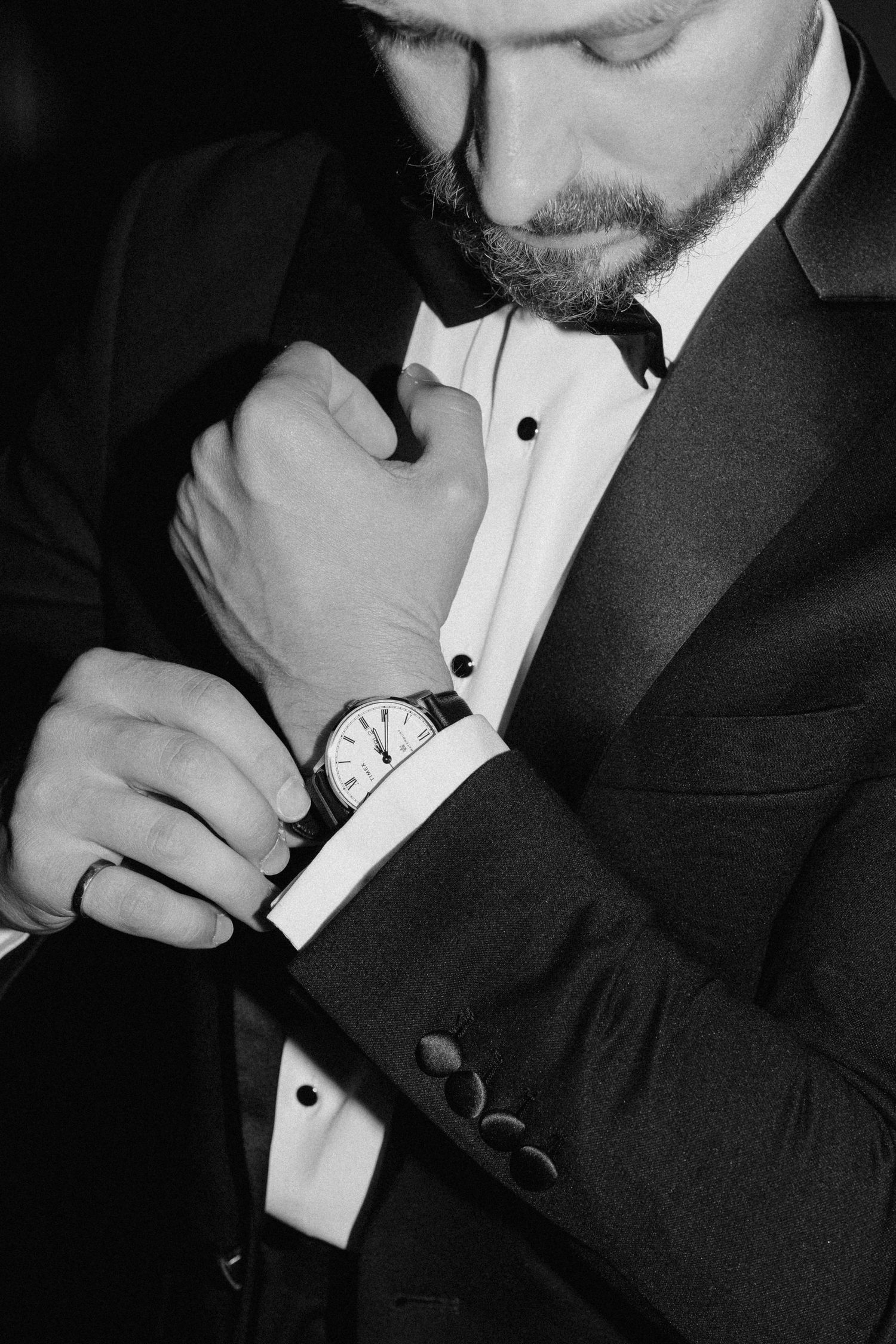 Groom in black tuxedo adjusting his watch cufflink in black and white photo at Pillar and Post.