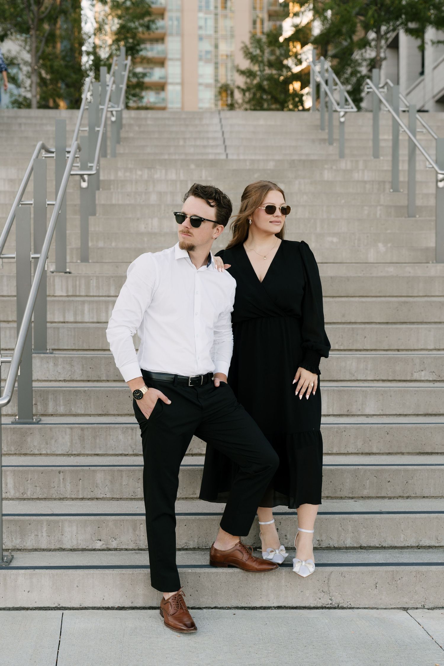 Stylish couple in black and white outfits posing on outdoor staircase with sunglasses.