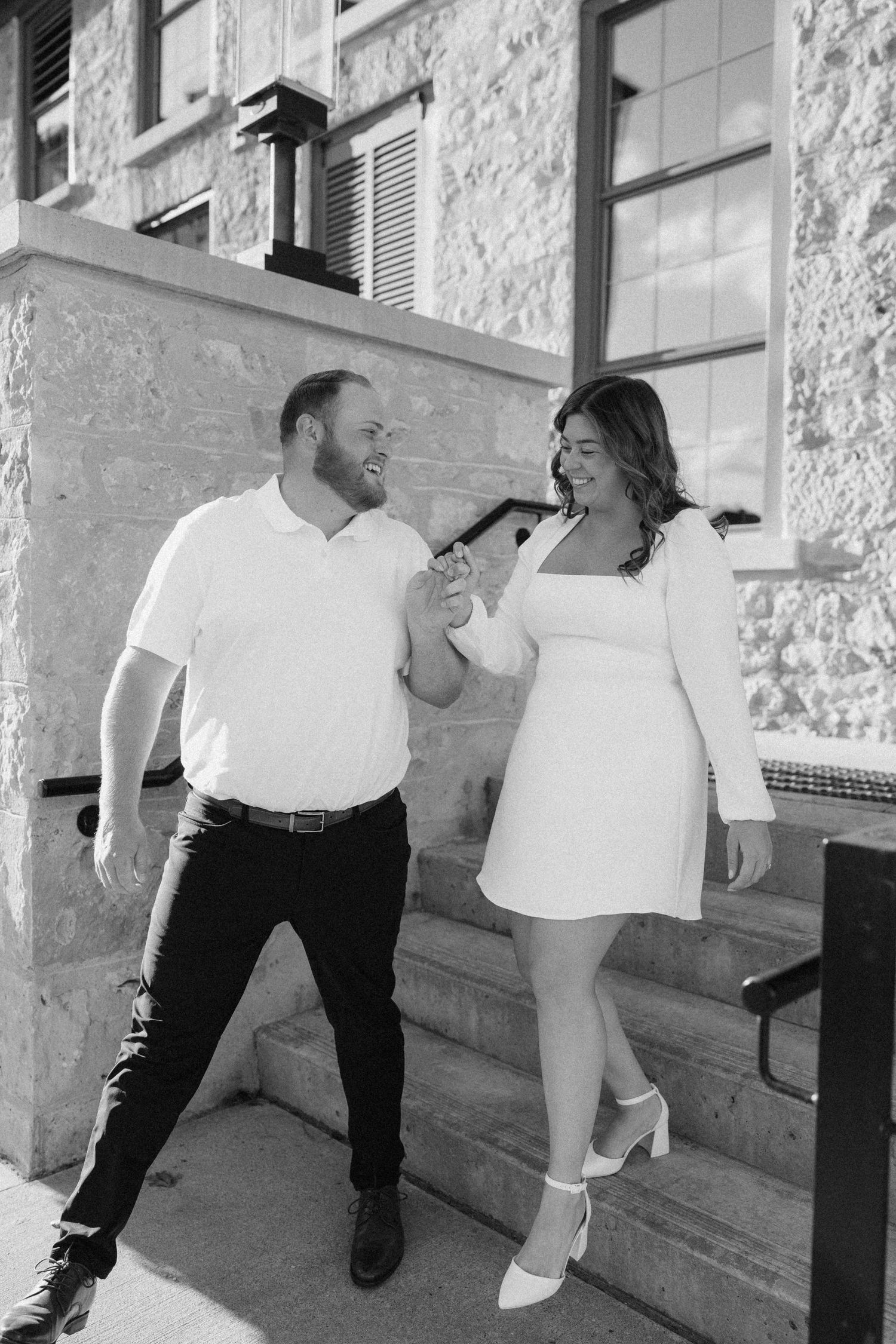 Black and white photo of laughing couple holding hands on outdoor stone steps.