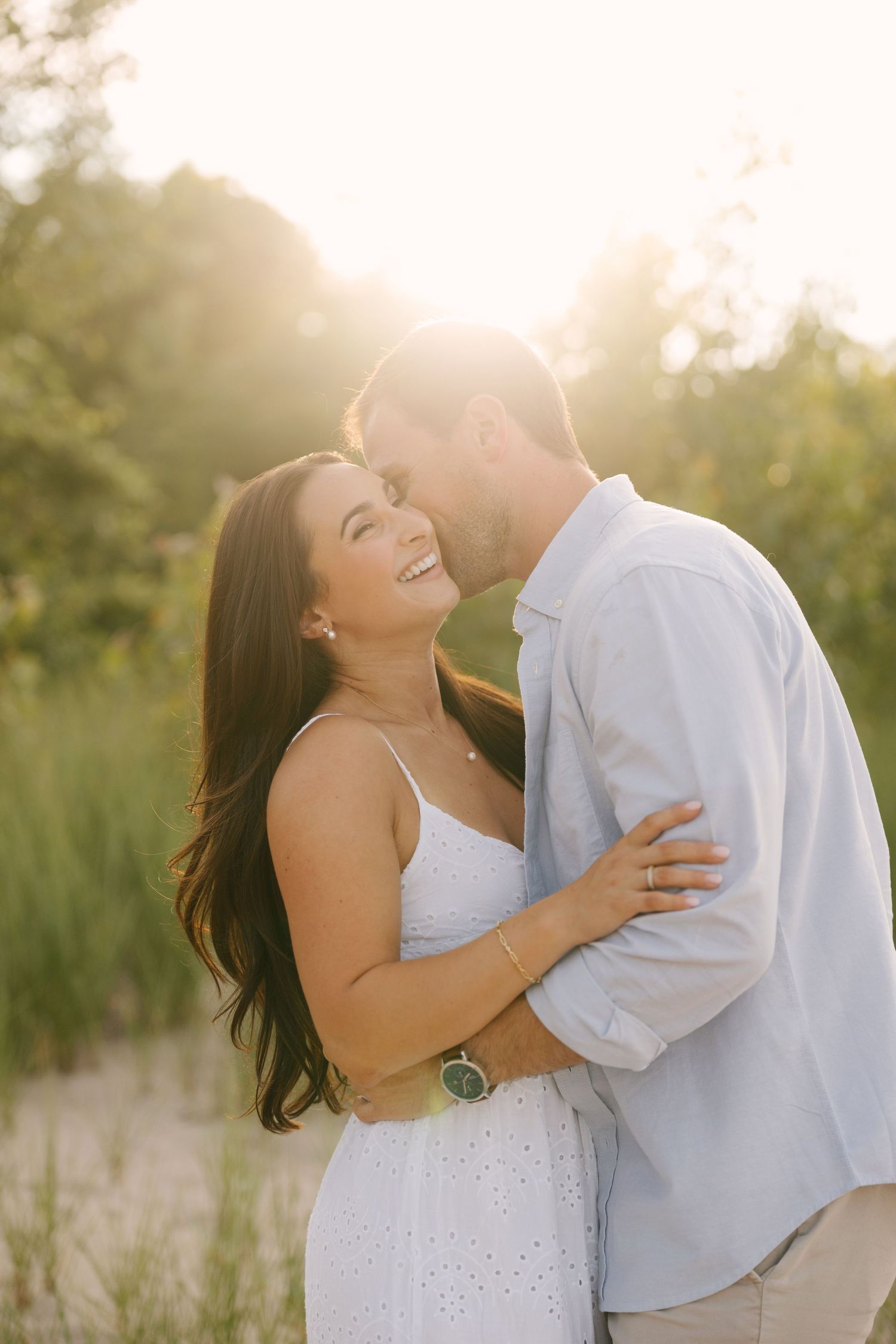 Woman laughing as man kisses her cheek in glowing golden sunset outdoors.