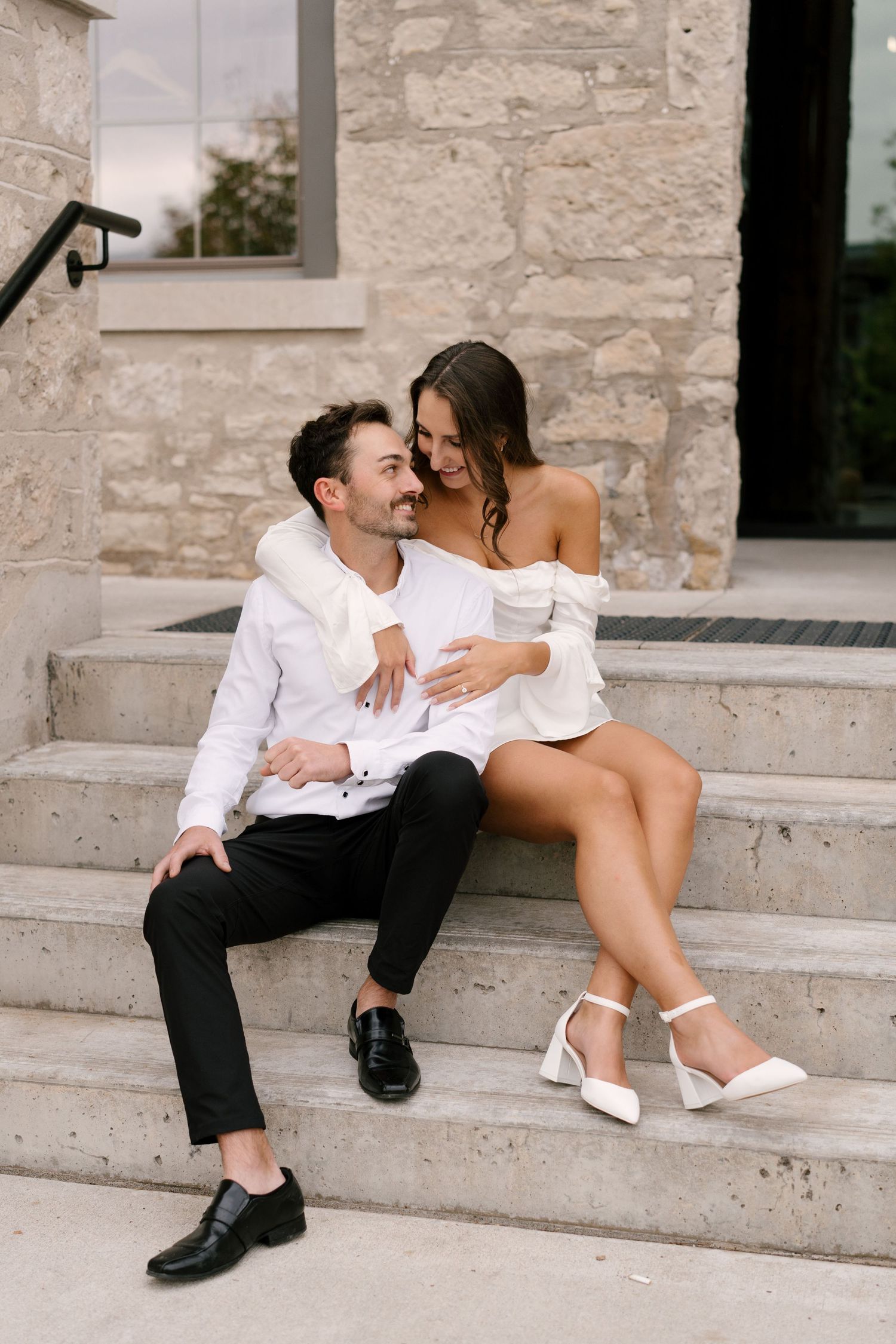 Happy couple sitting together on stone steps, laughing and embracing outdoors.
