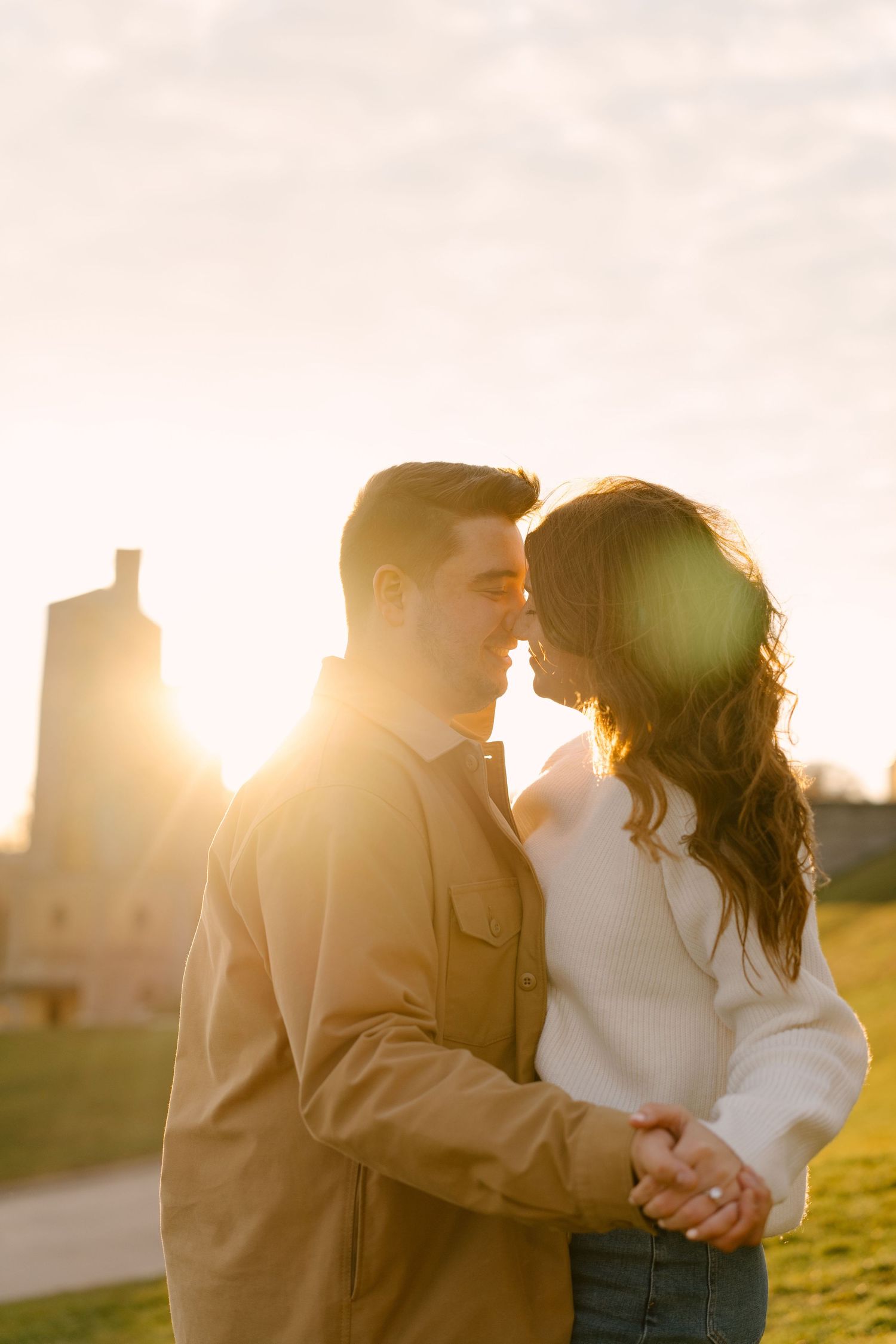 Romantic couple about to kiss while embracing at stunning golden sunset with lens flare outdoors.