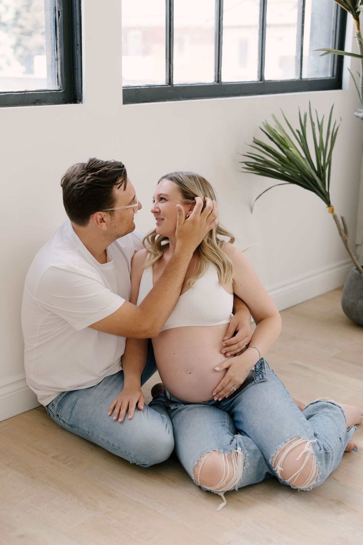 Couple sitting on floor smiling at each other, man gently holding pregnant womans face near her bump.