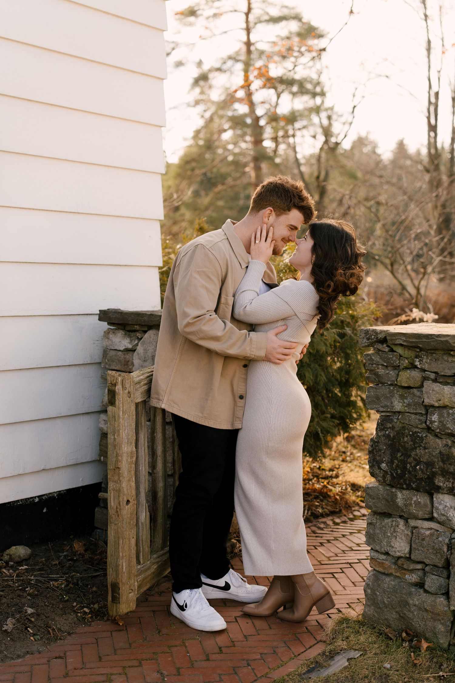 Romantic couple embracing and kissing beside a white building with stone wall outdoors.