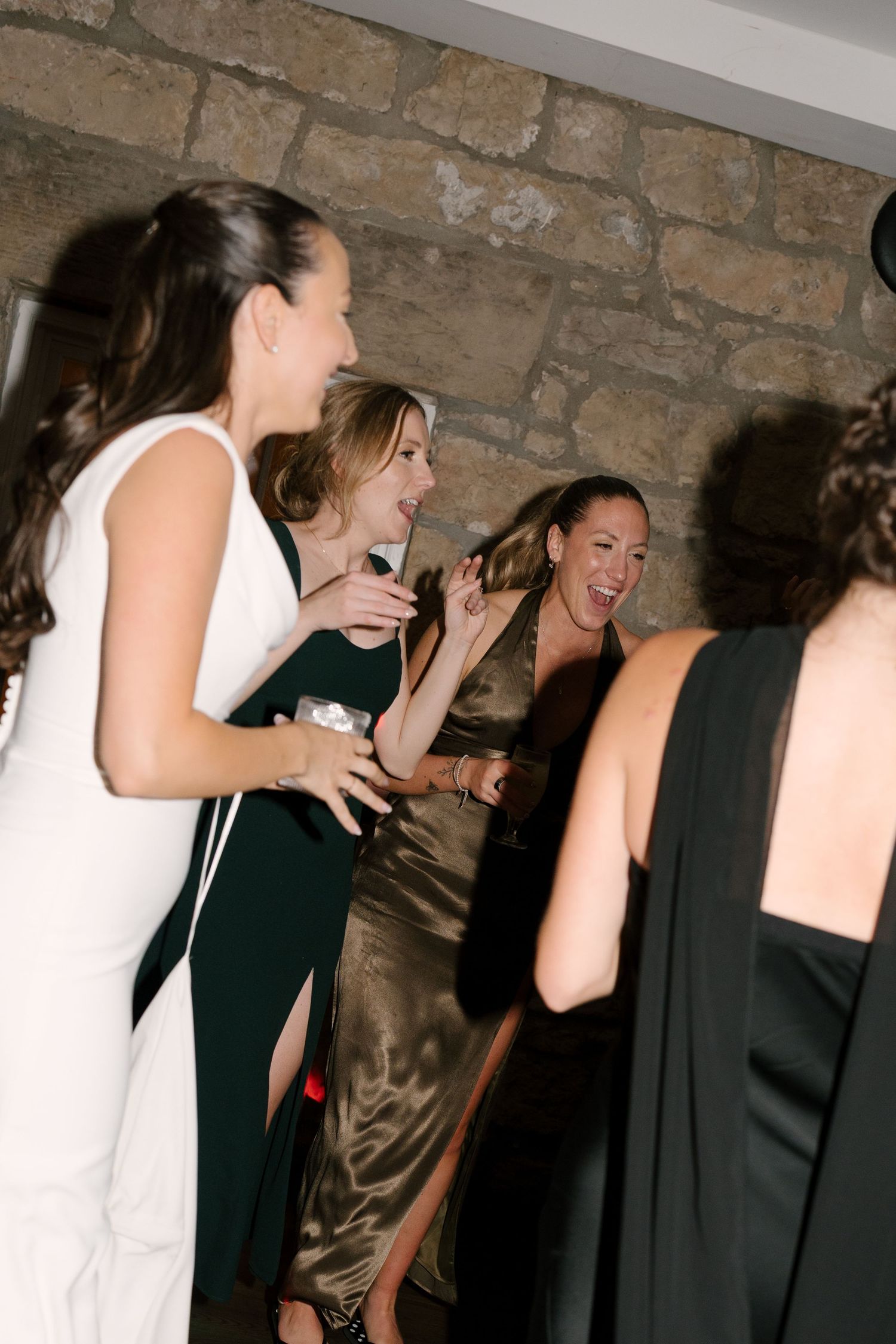 Group of women in formal gowns laughing and dancing joyfully at a wedding reception.