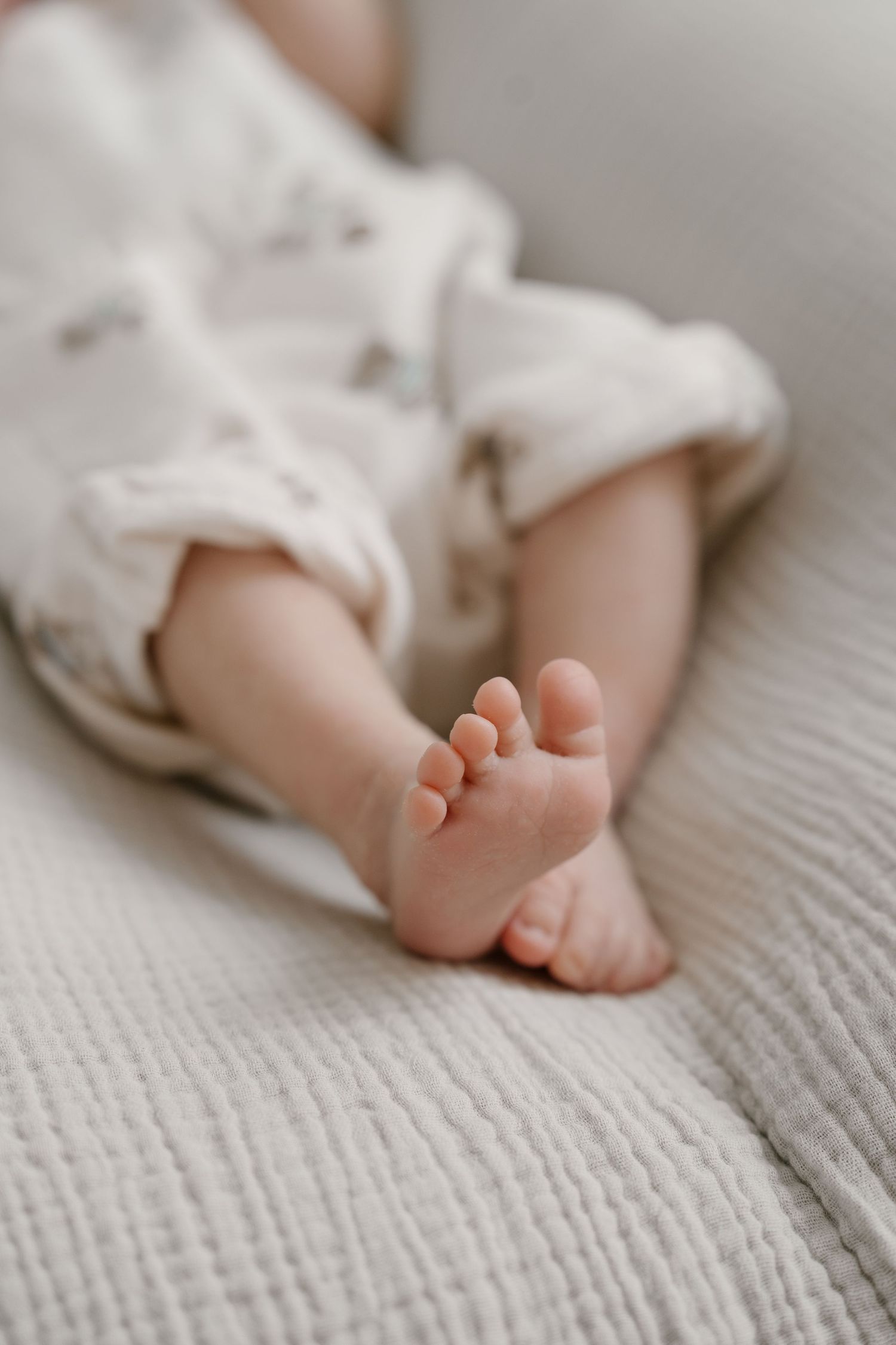 Tiny newborn baby feet resting on soft white textured blanket.
