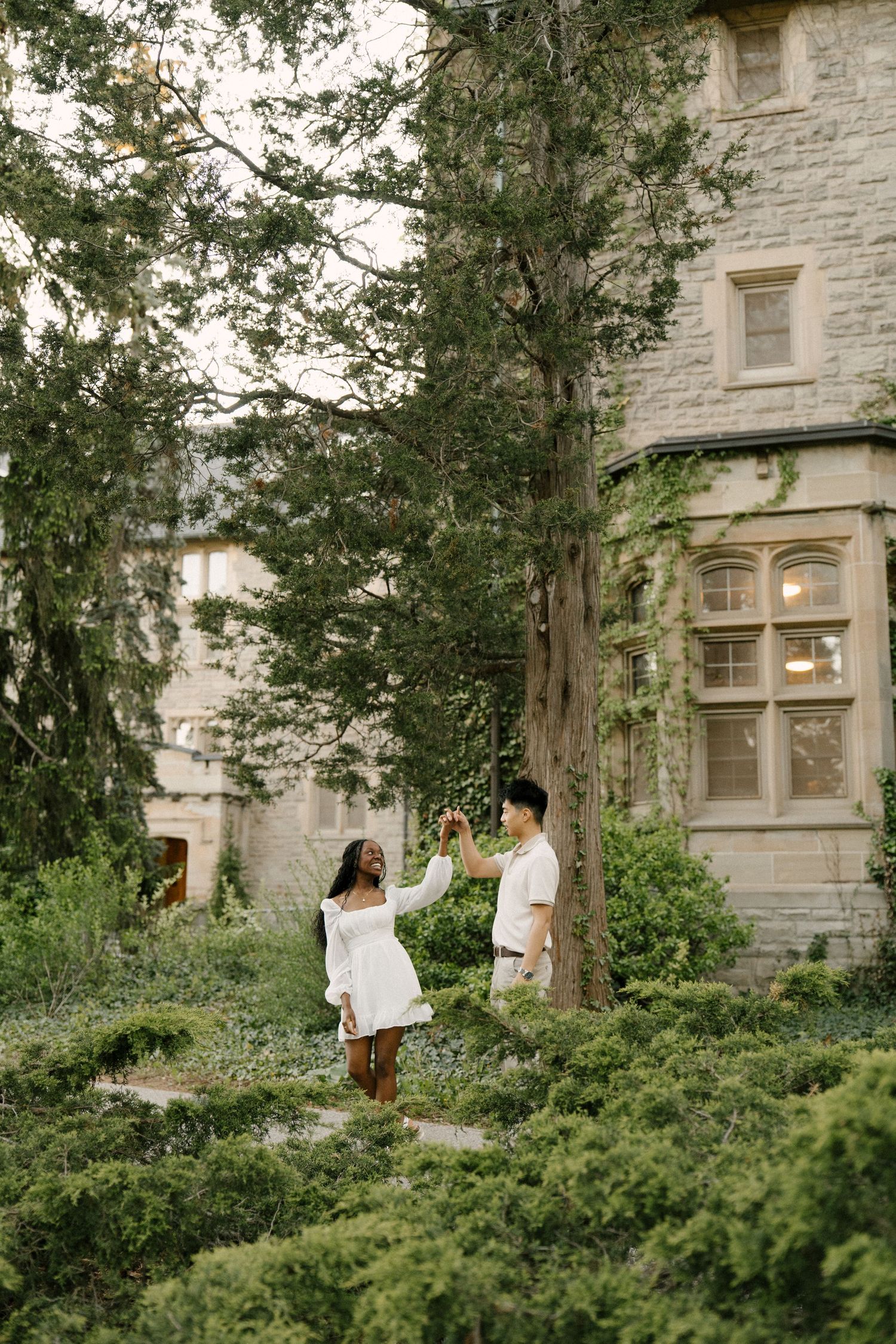 Couple dancing together in a lush garden beside an ivy-covered stone building.