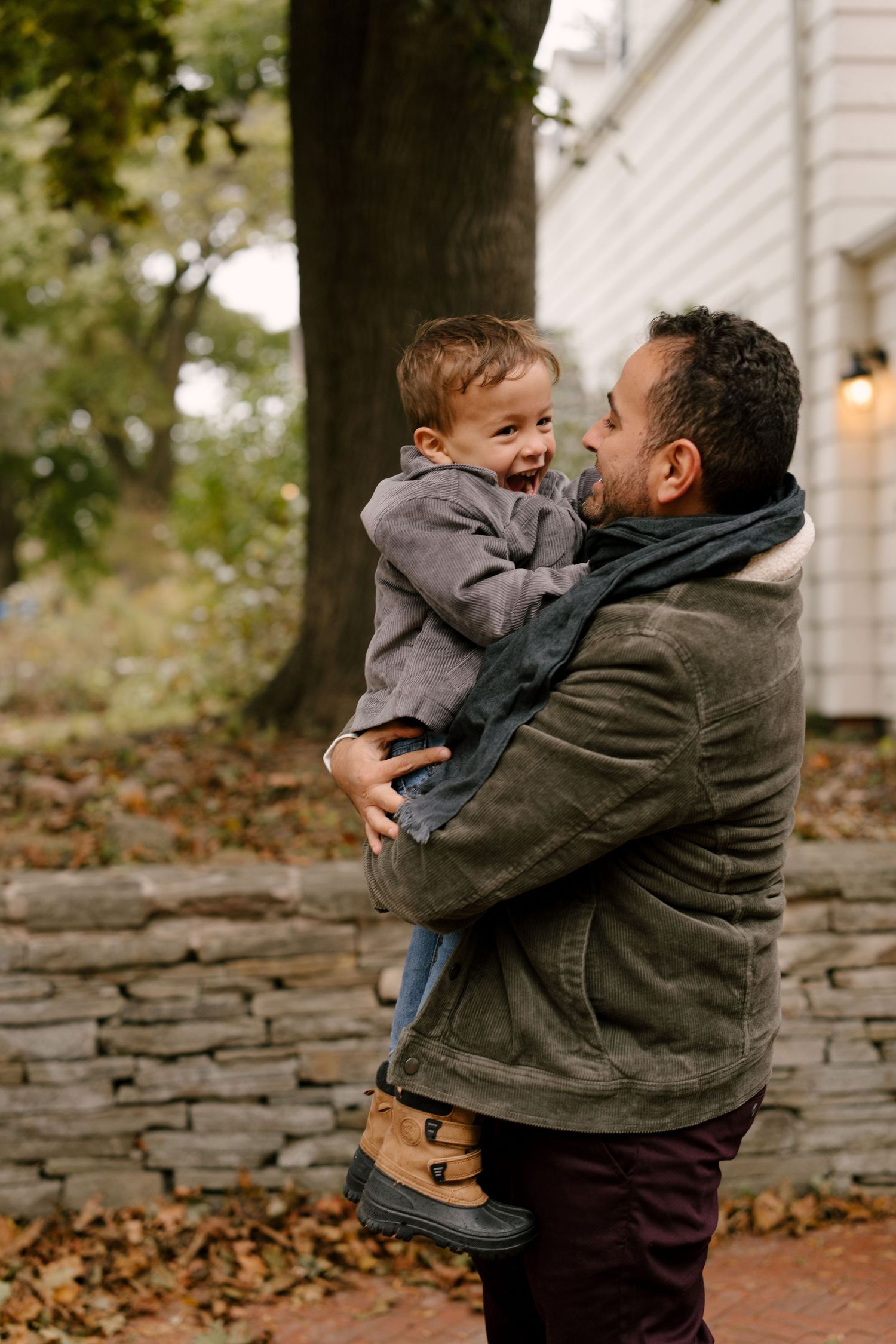 Father in green jacket lovingly holding giggling toddler son in autumn outdoor setting.