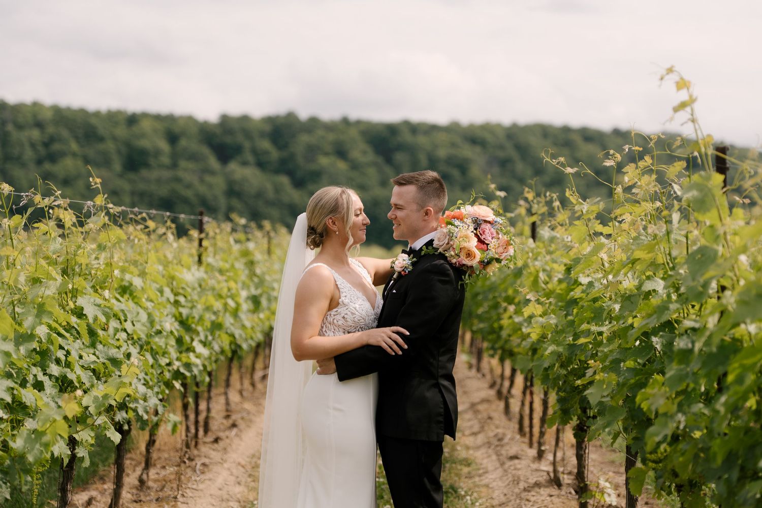 Bride and groom share intimate moment smiling at each other between vineyard rows at Niagara on the lake.
