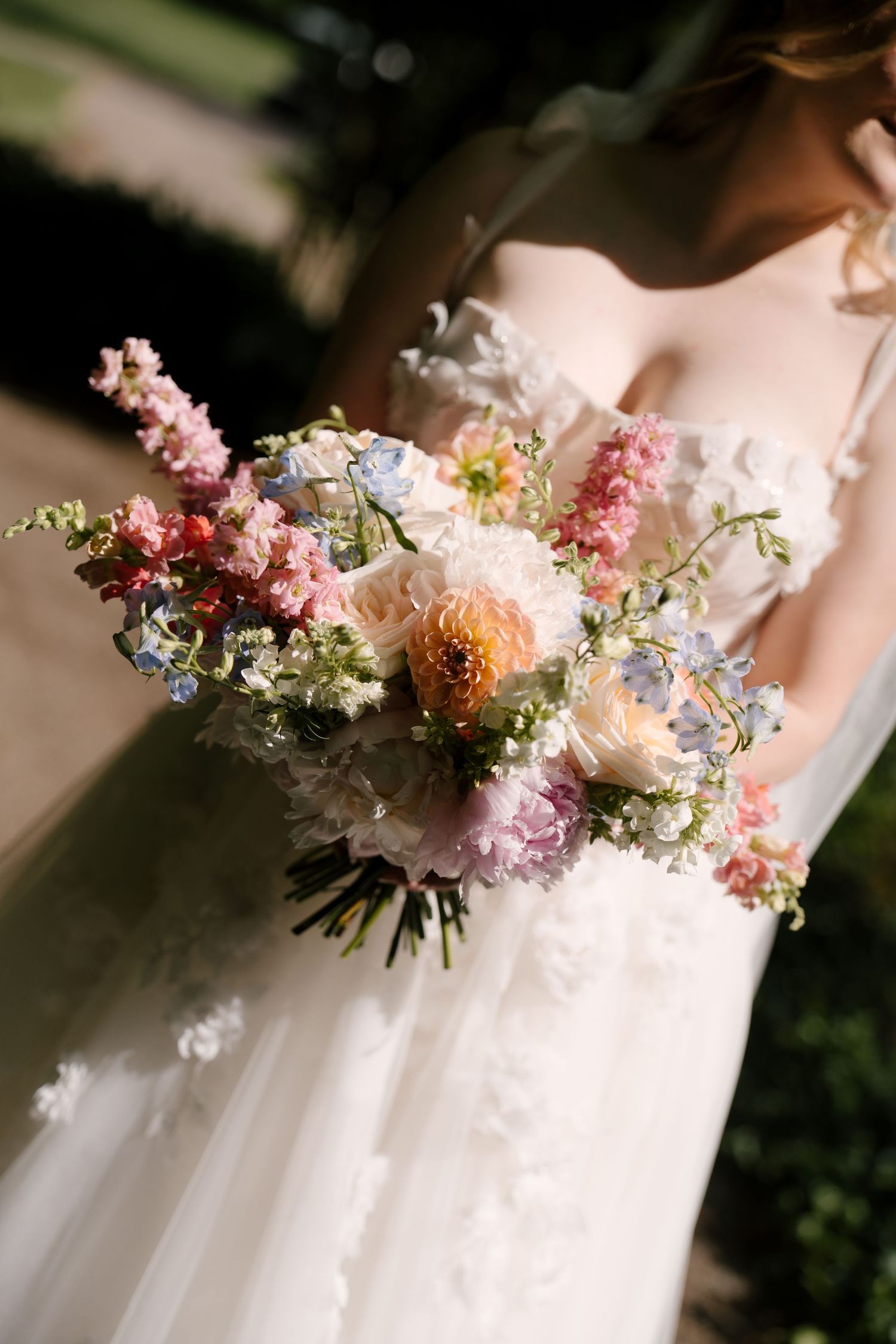Bride in white floral gown holding colorful spring wedding bouquet with peonies and snapdragons.