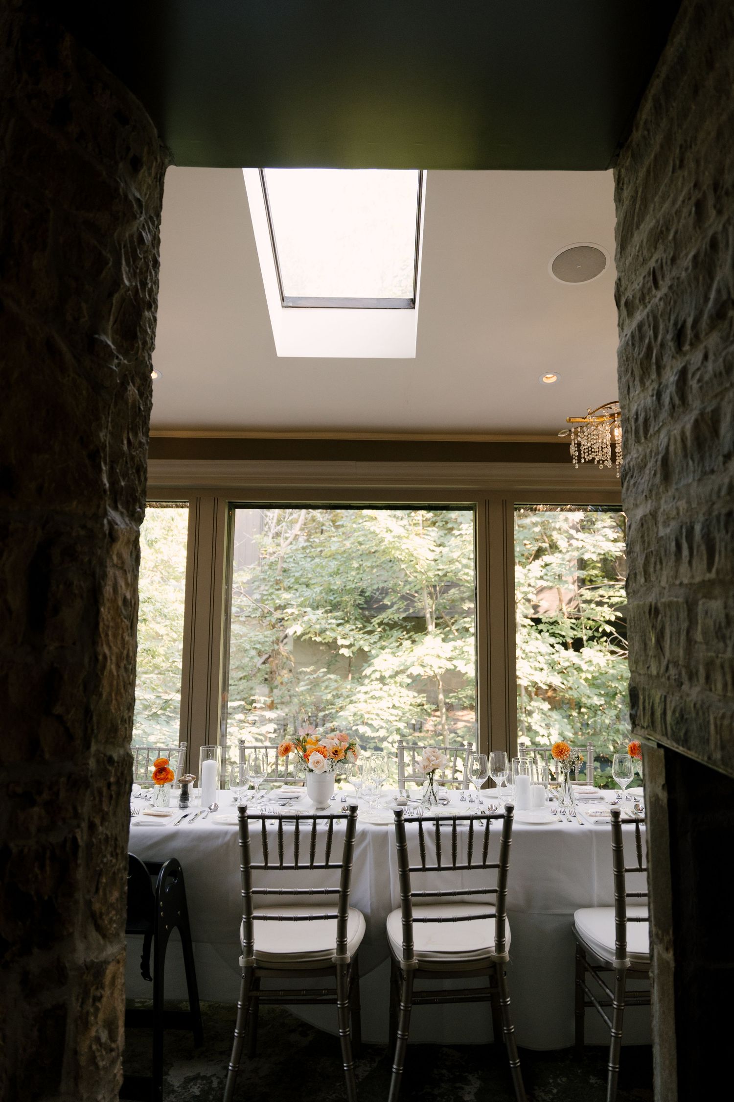 Intimate Ancaster Mill wedding dining room with stone walls, skylight, and lush garden views through large windows.
