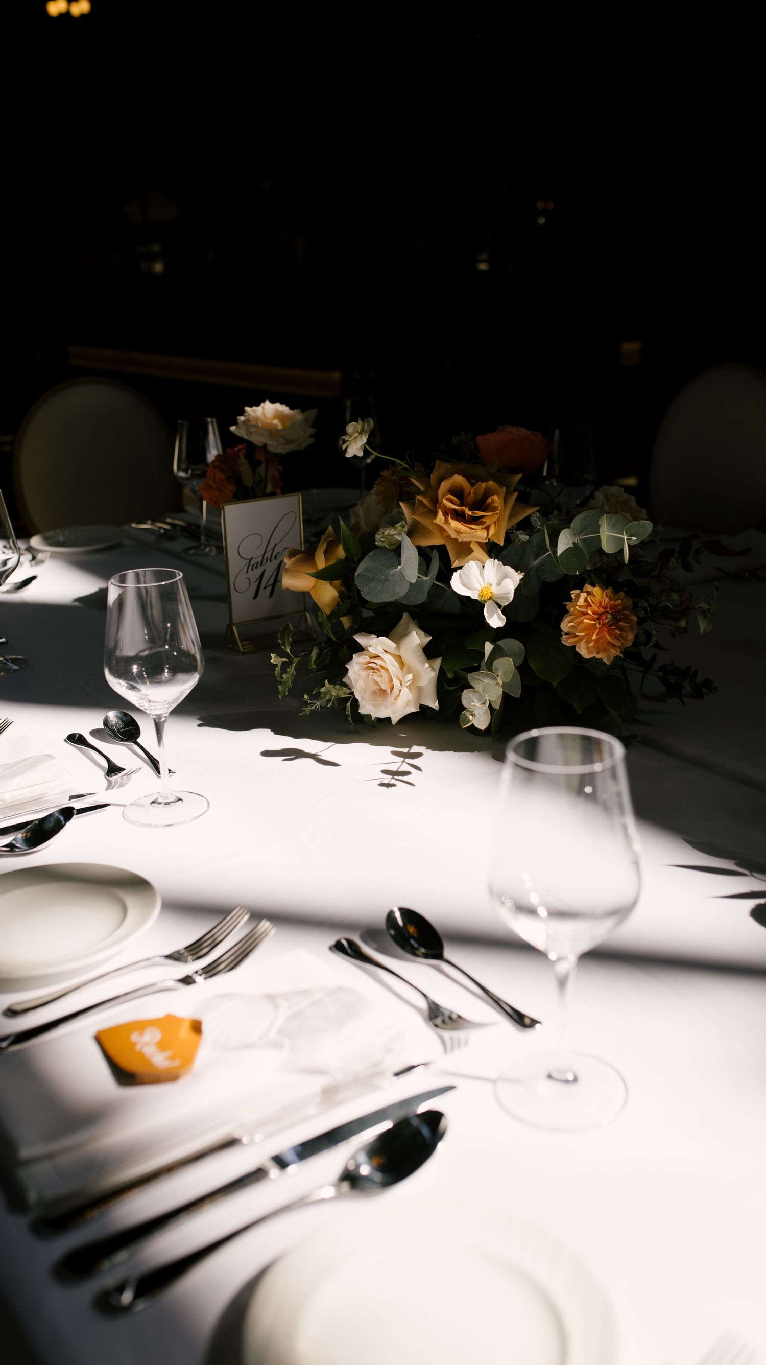 Elegant wedding table setting with white plates, crystal glasses, silverware, and warm-toned floral centerpiece.