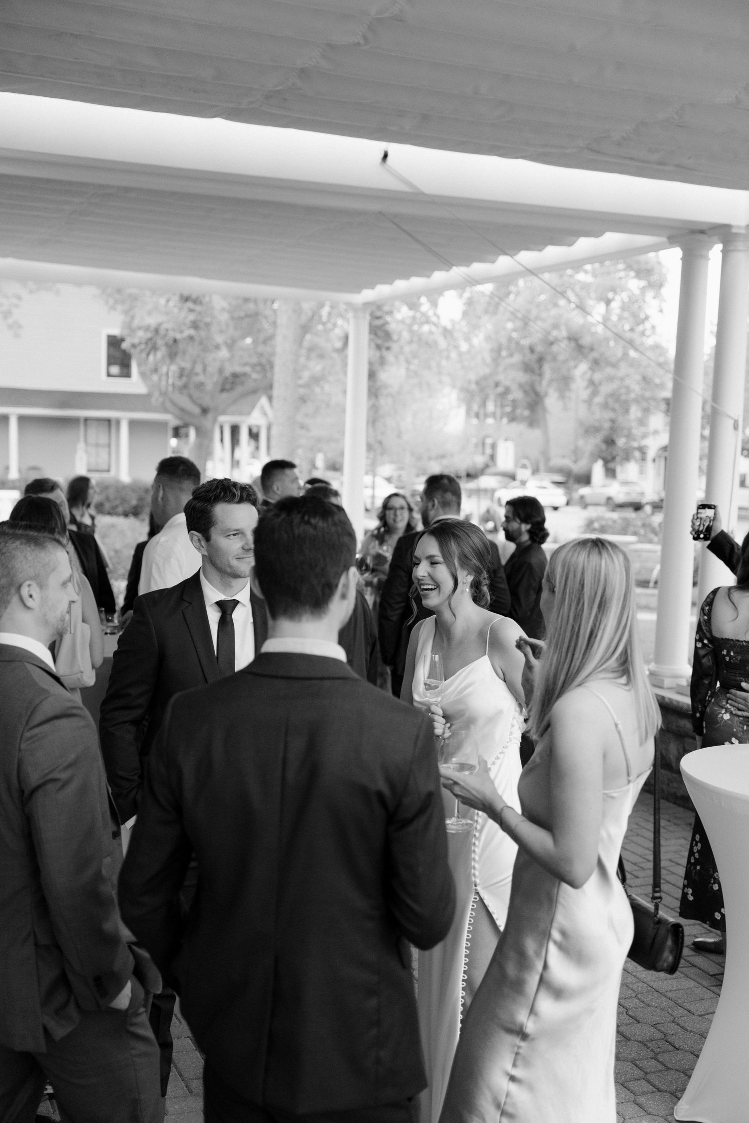 Black and white photo of bride laughing with wedding guests during outdoor cocktail hour at The Gate House venue.