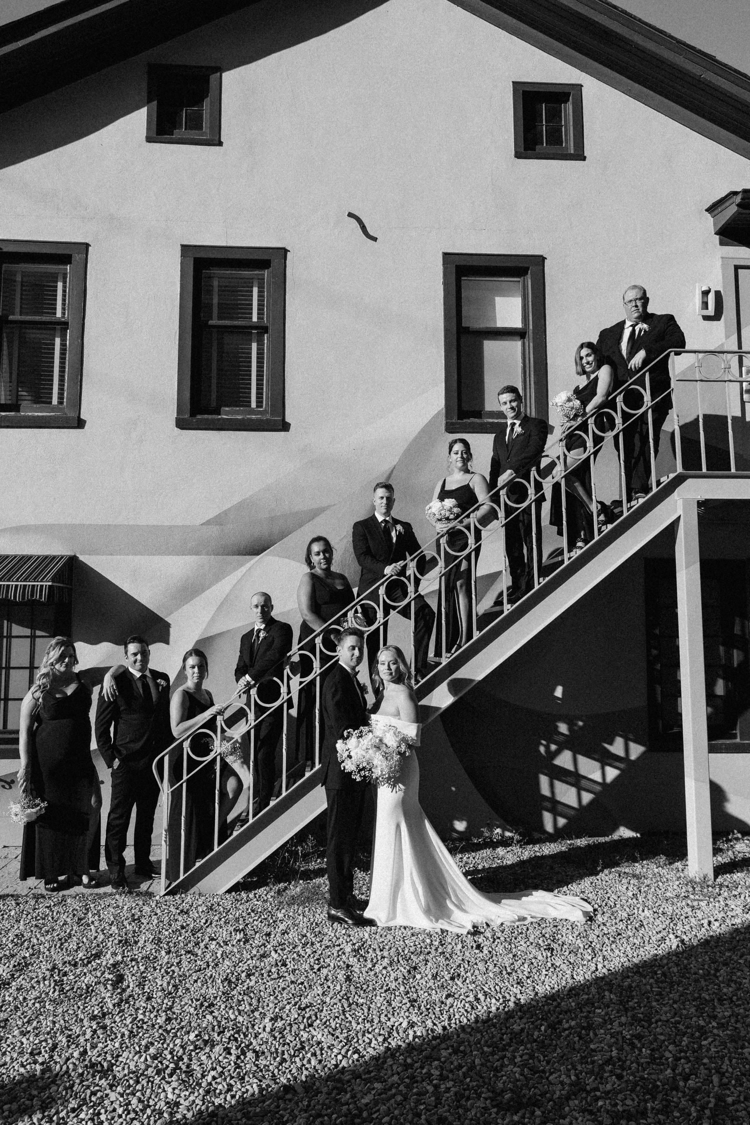 Wedding party posing on outdoor staircase of a venue in a classic black and white portrait.