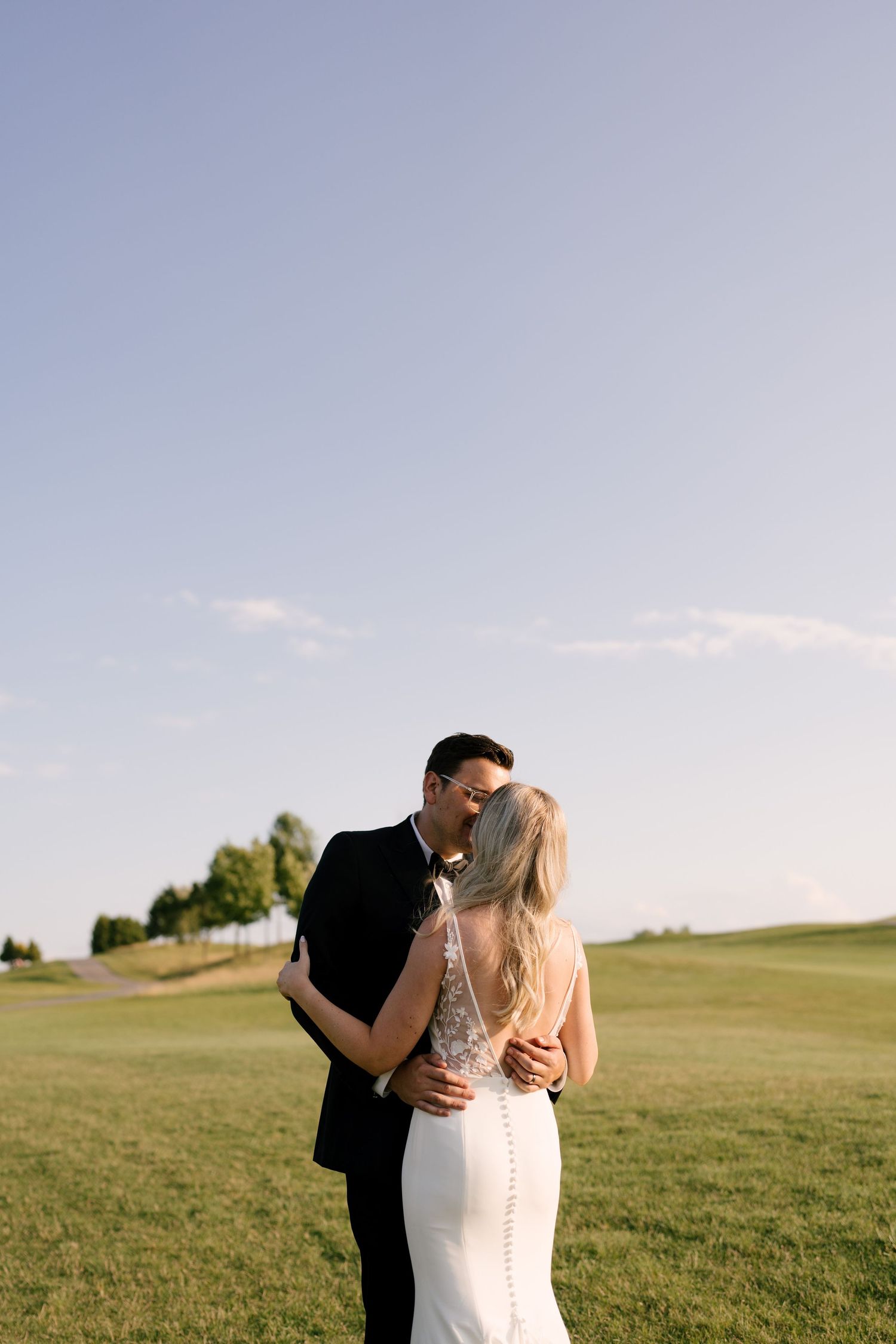 Bride and groom sharing a romantic kiss on a green Whistle Bear golf course under a clear blue sky.