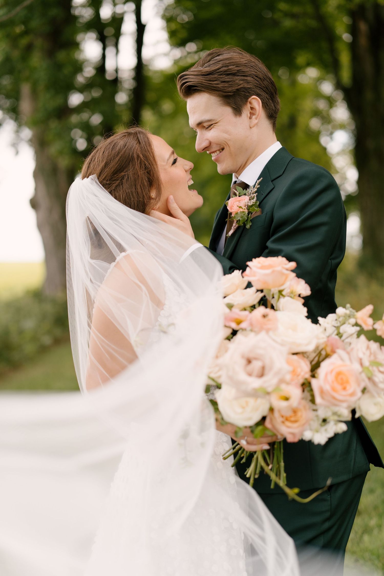 Bride and groom gazing at each other lovingly as wedding veil flows in outdoor portrait.
