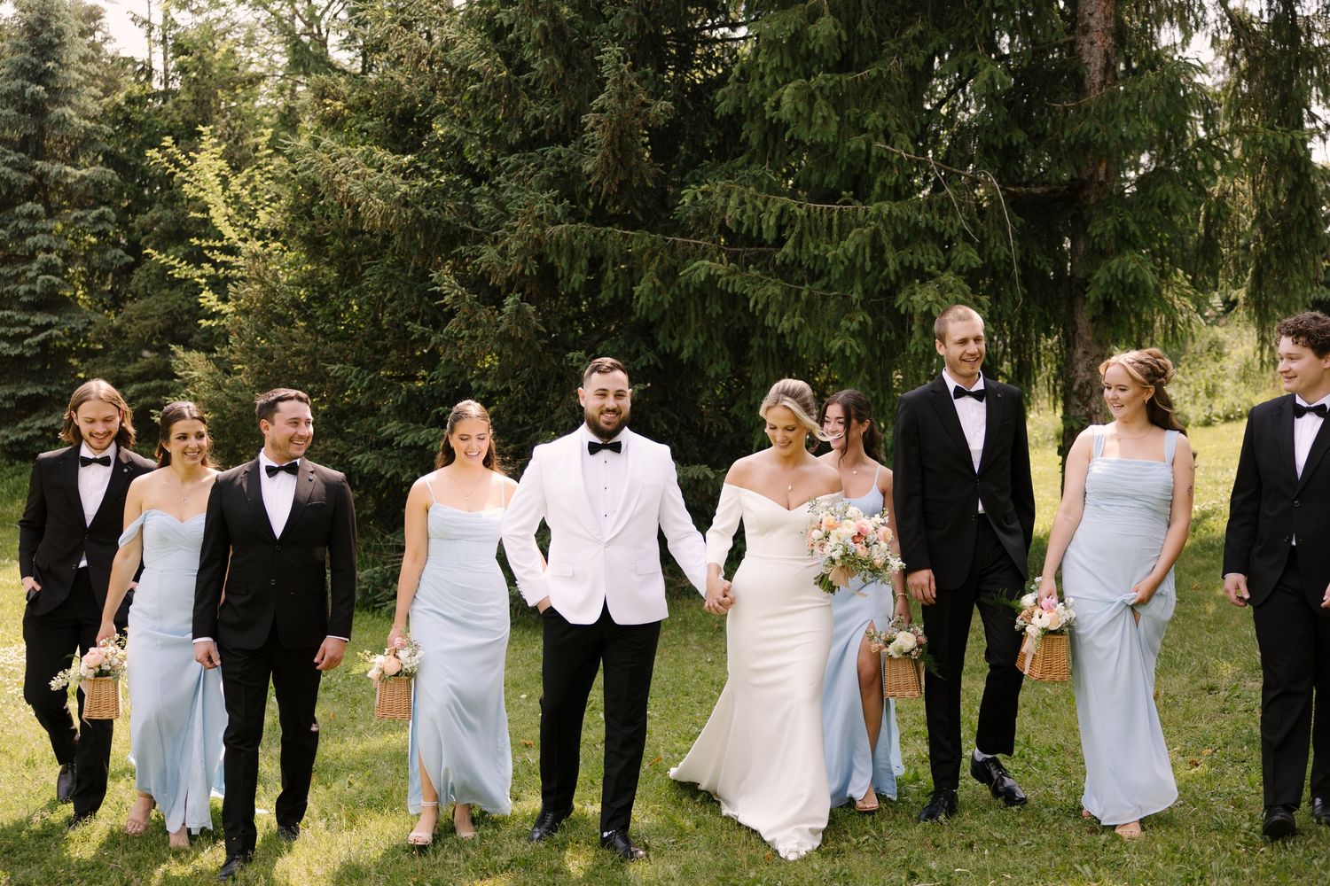Wedding party walking together outdoors, bridesmaids in light blue gowns, groomsmen in black tuxedos, bride and groom in center.