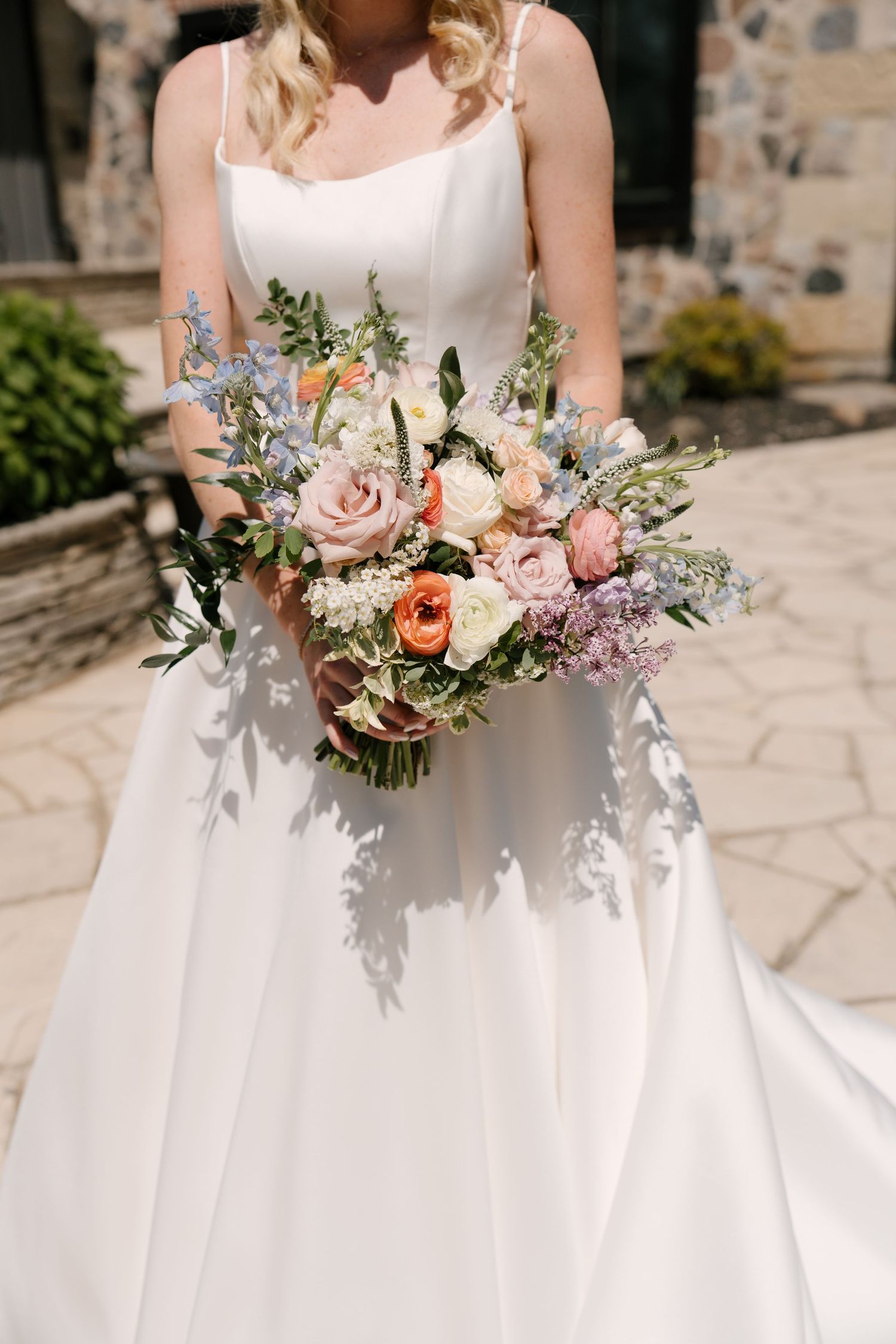 Bride in white spaghetti strap gown holds colorful bouquet with pink, orange, and blue blooms.