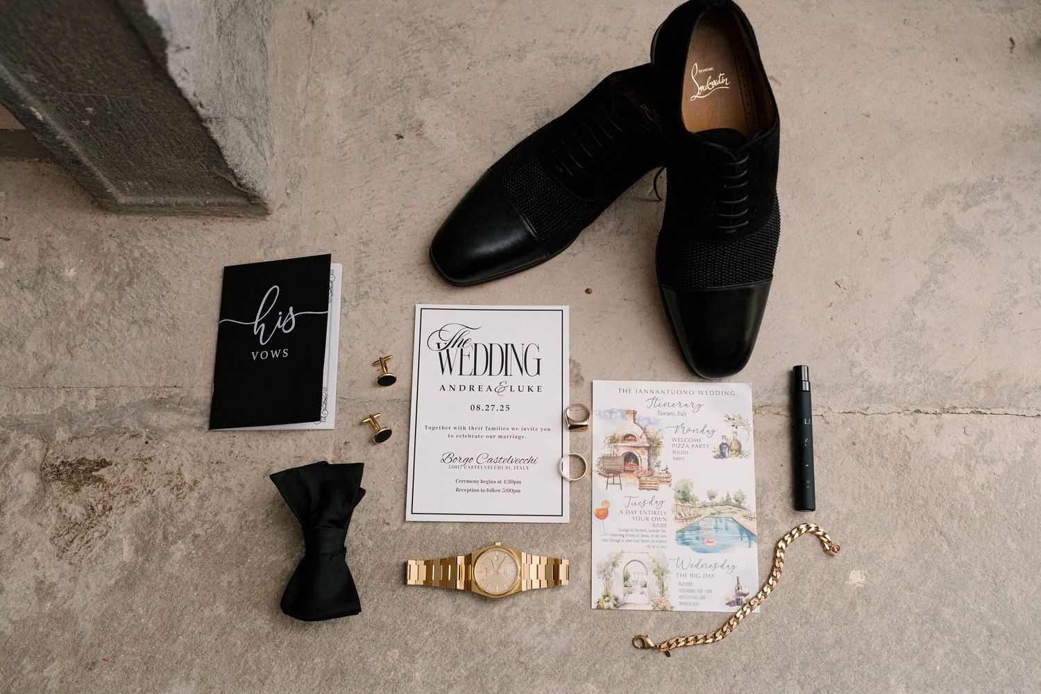 Groom wedding flat lay with black Oxford shoes, bow tie, gold watch, invitation suite, and vows book on stone floor.