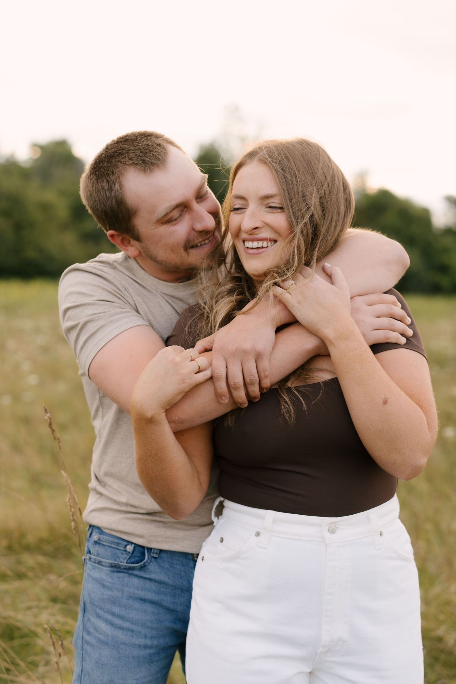 Happy couple embracing in a golden sunlit field, woman laughing joyfully.