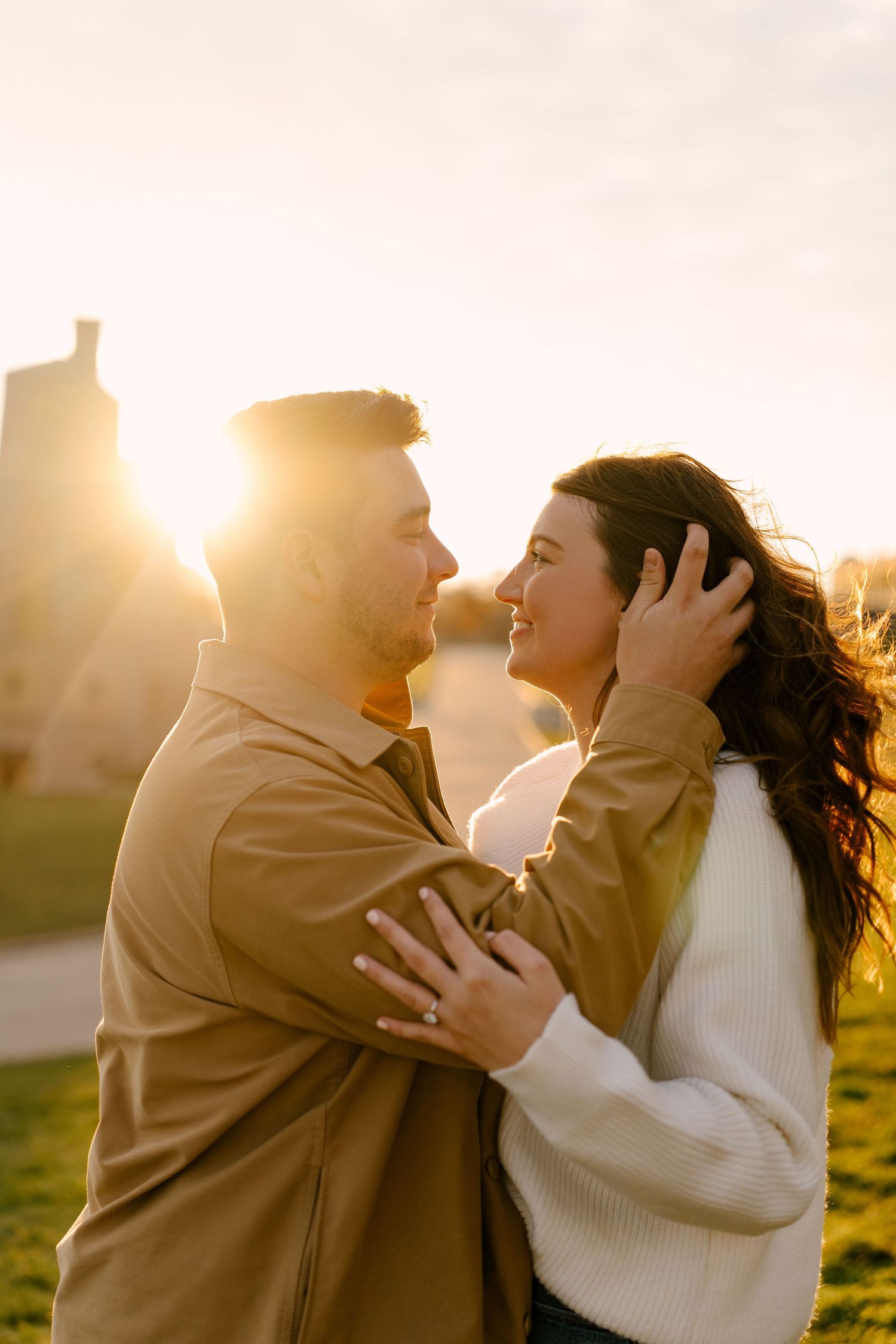 Couple embracing face-to-face at golden hour sunset, woman touching mans face tenderly outdoors.