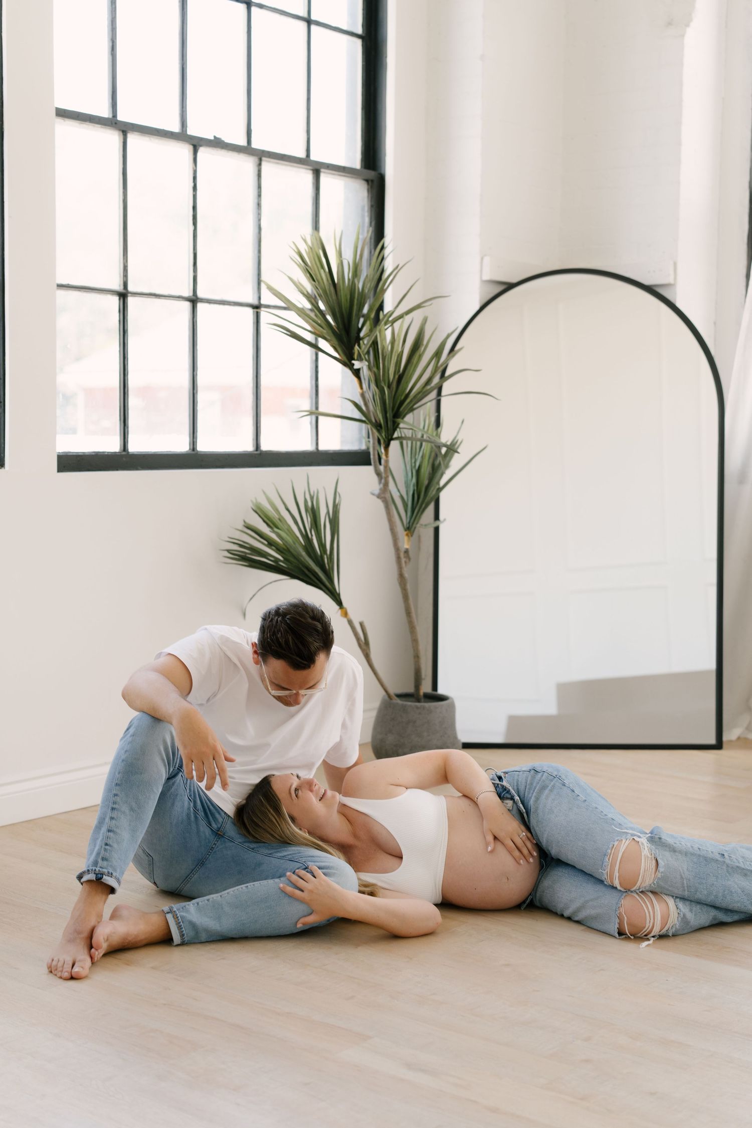 Man and pregnant woman relaxing on hardwood floor, woman lying back while partner gazes at her bump.