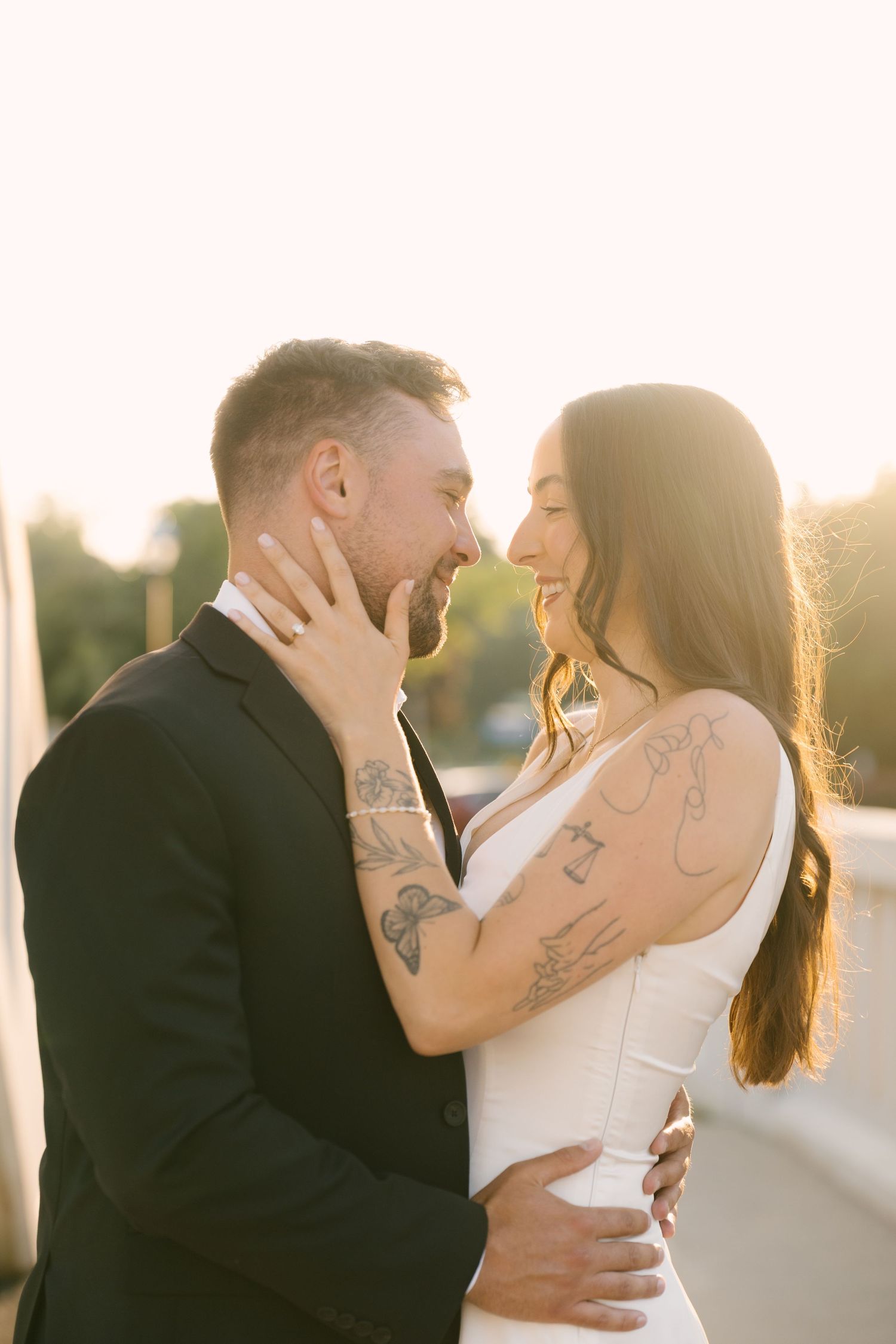 Tattooed couple embracing and about to kiss in warm golden sunset light outdoors.