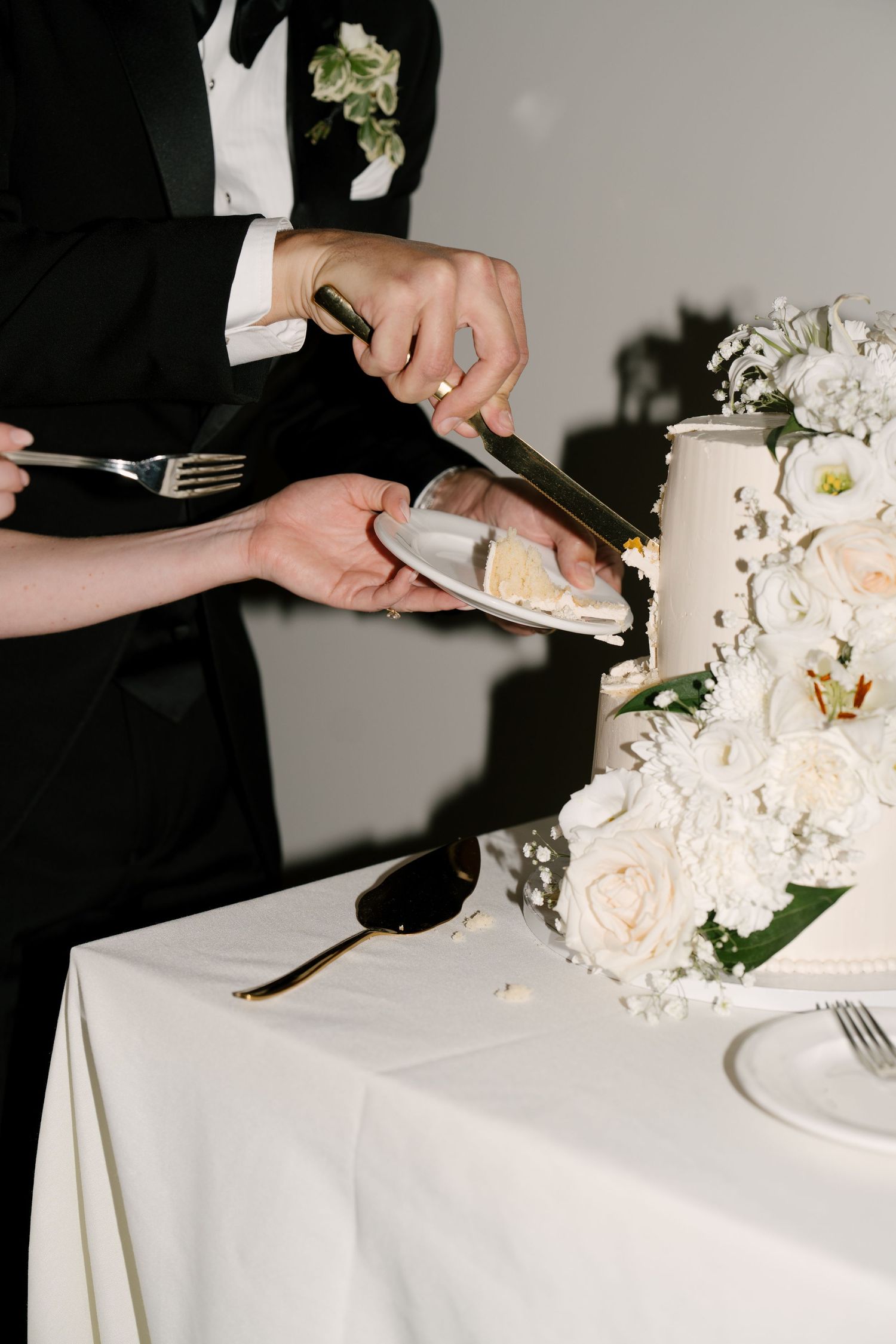 Close-up of bride and groom cutting a white multi-tiered wedding cake adorned with roses.