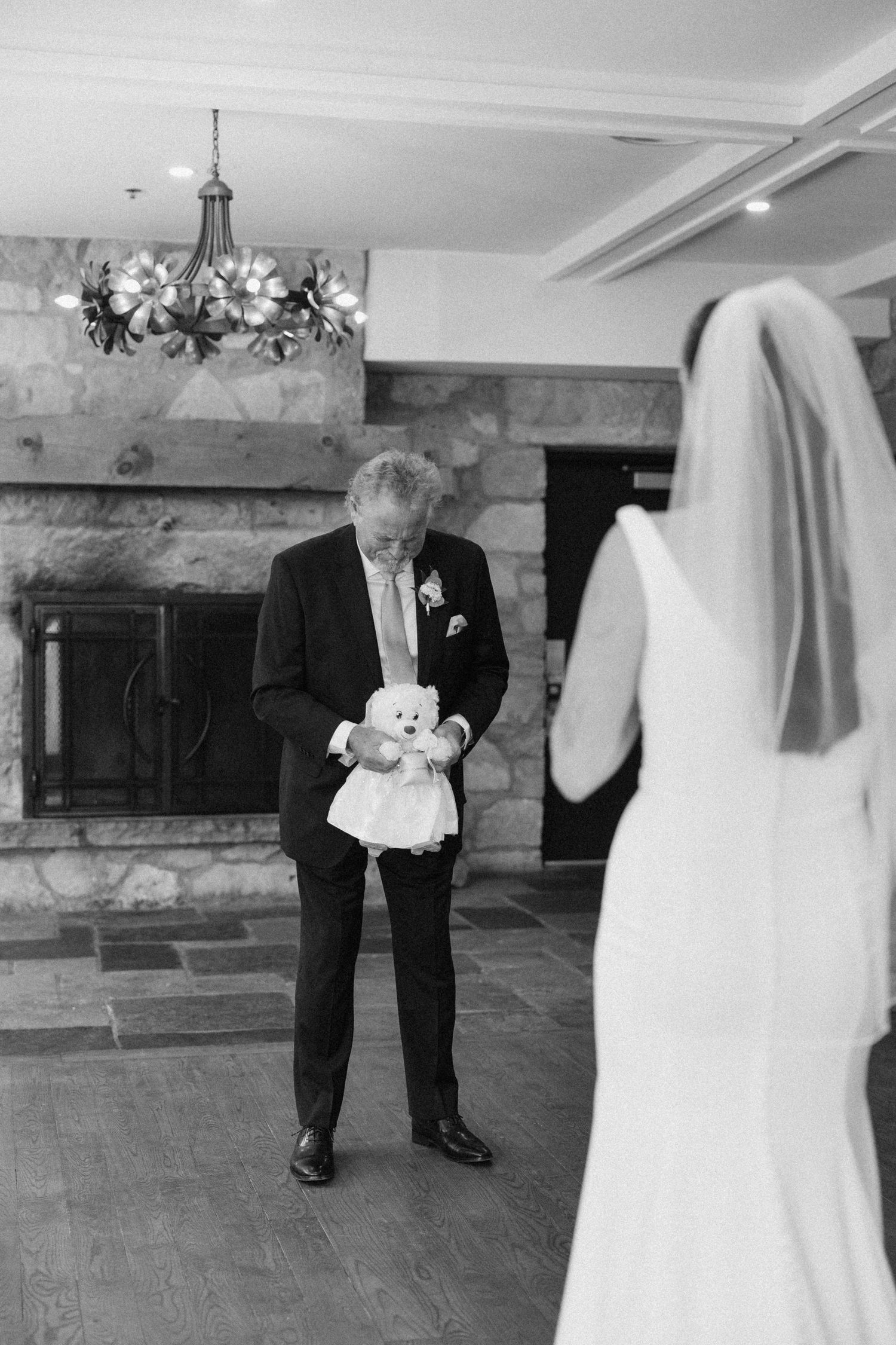 Emotional father seeing his daughter in her wedding dress for the first time, holding a stuffed bear.