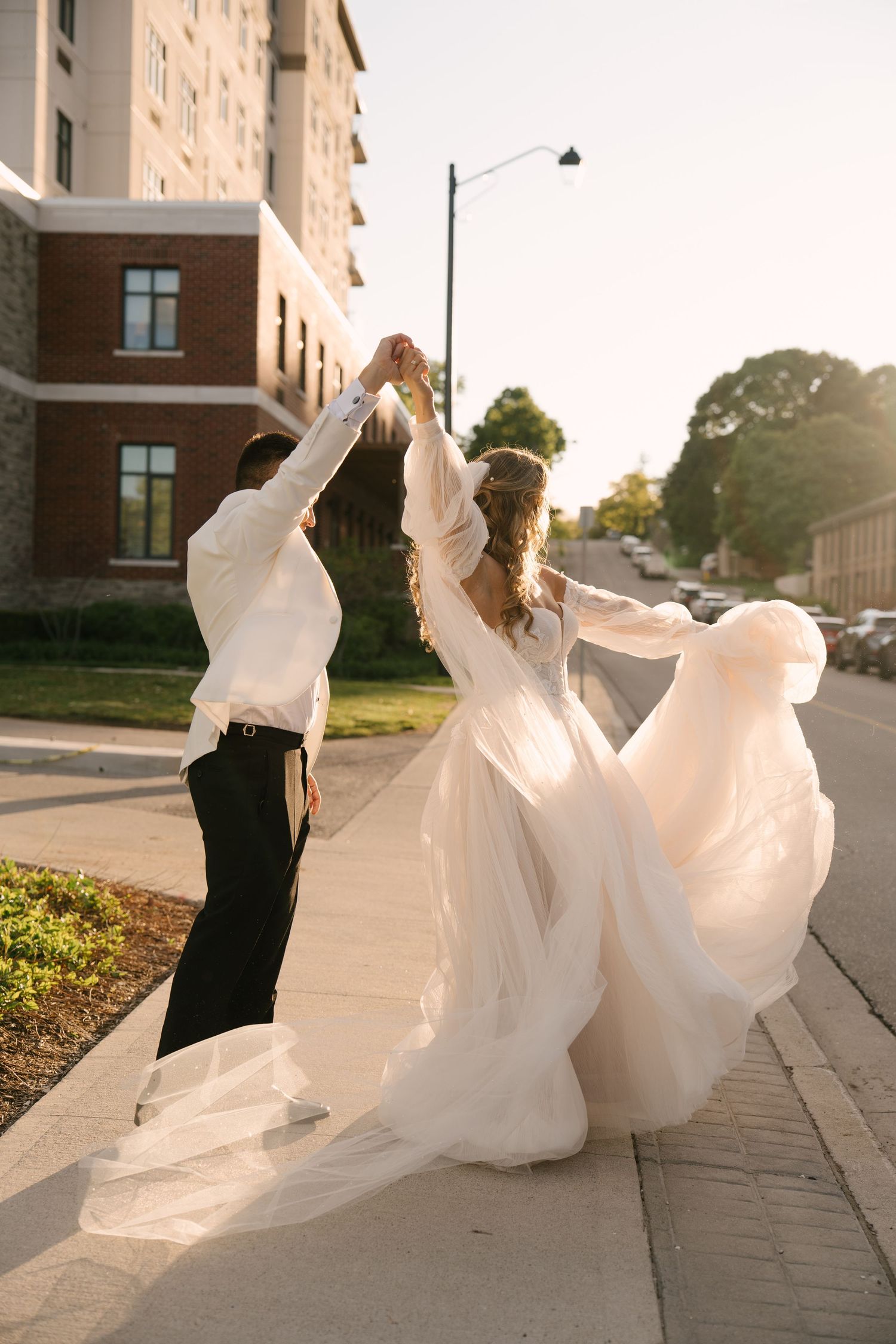 Bride and groom dancing on sidewalk in golden hour sunlight, wedding dress flowing gracefully outside Tapestry Hall wedding venue.