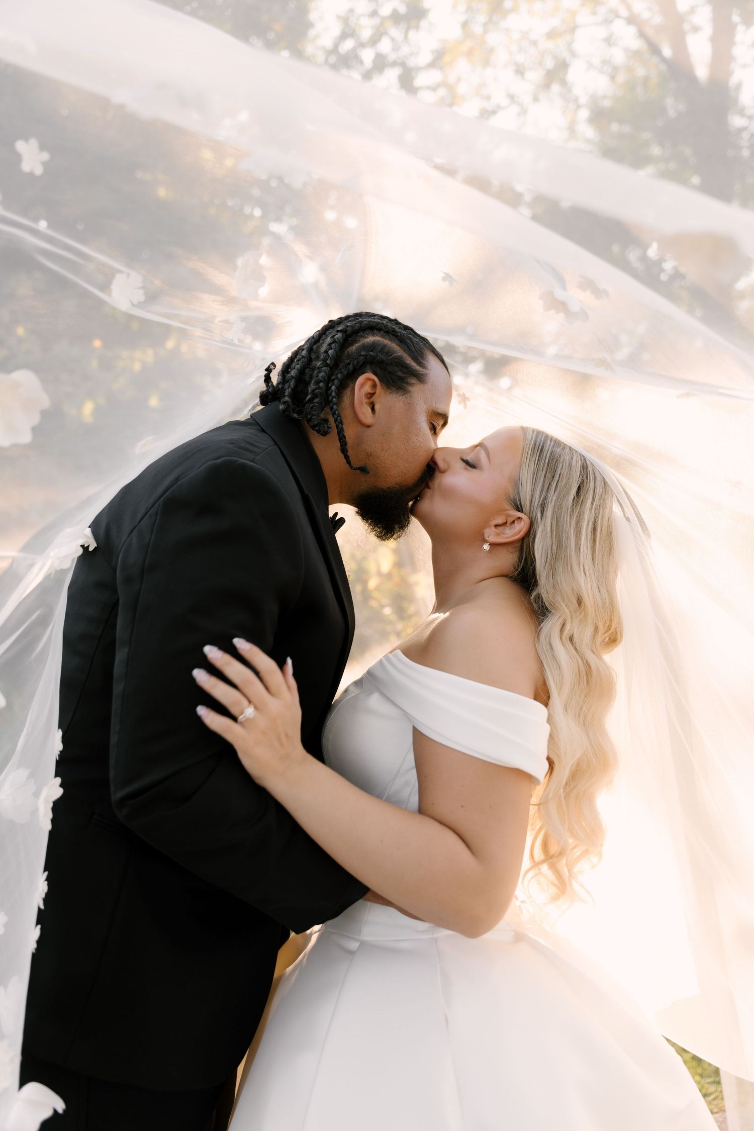 Bride and groom share romantic kiss under flowing floral veil in golden sunlight in Cambridge Ontario.