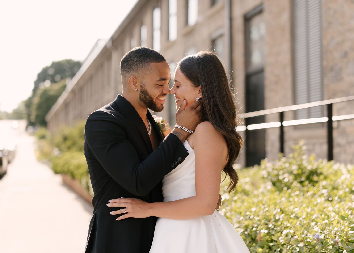 Bride and groom share a romantic close moment outdoors, groom in black suit, bride in white gown outside Tapestry Hall.