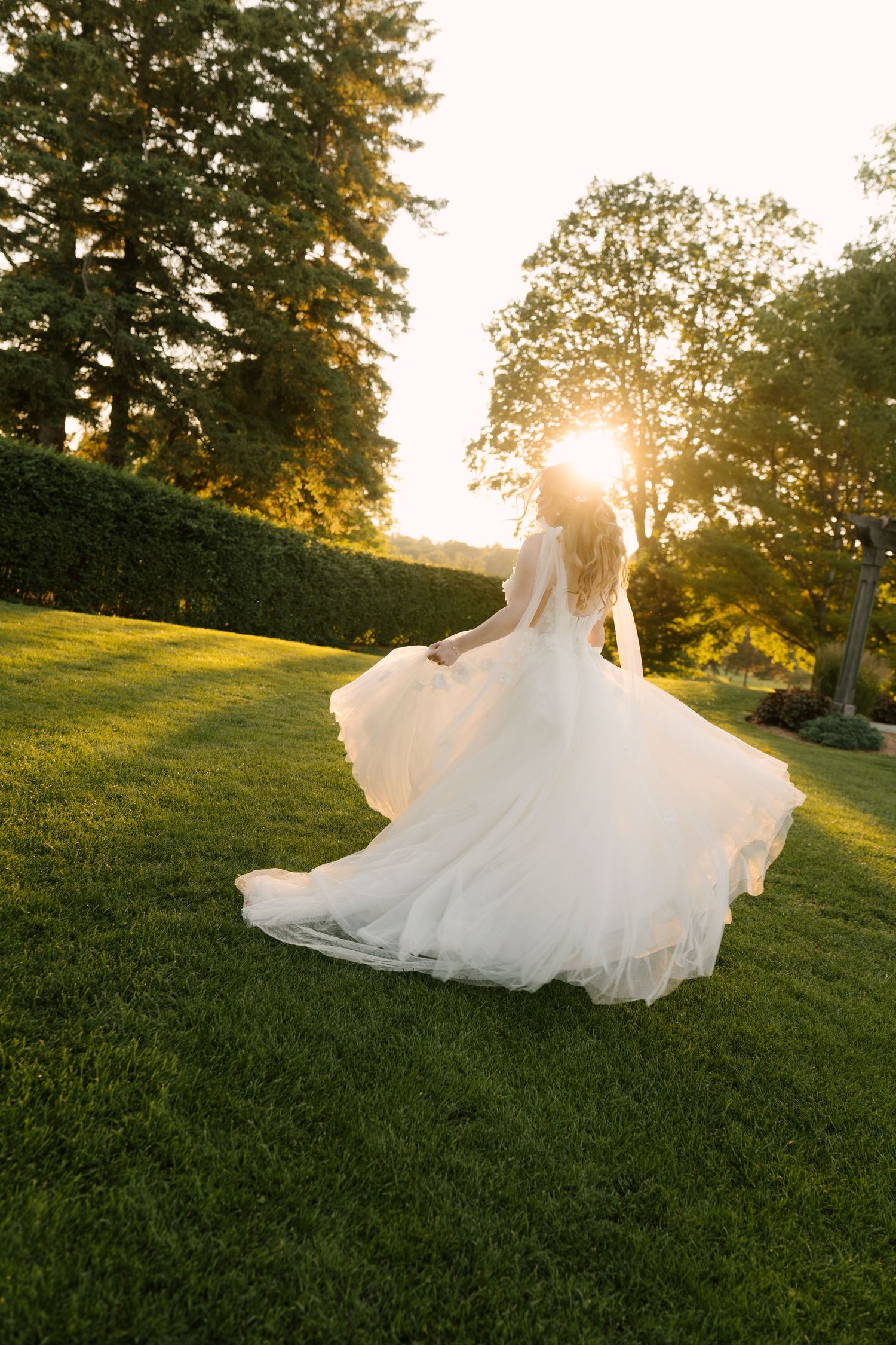 Bride in flowing white gown twirling at golden sunset on lush green lawn at St Marys Golf Club.