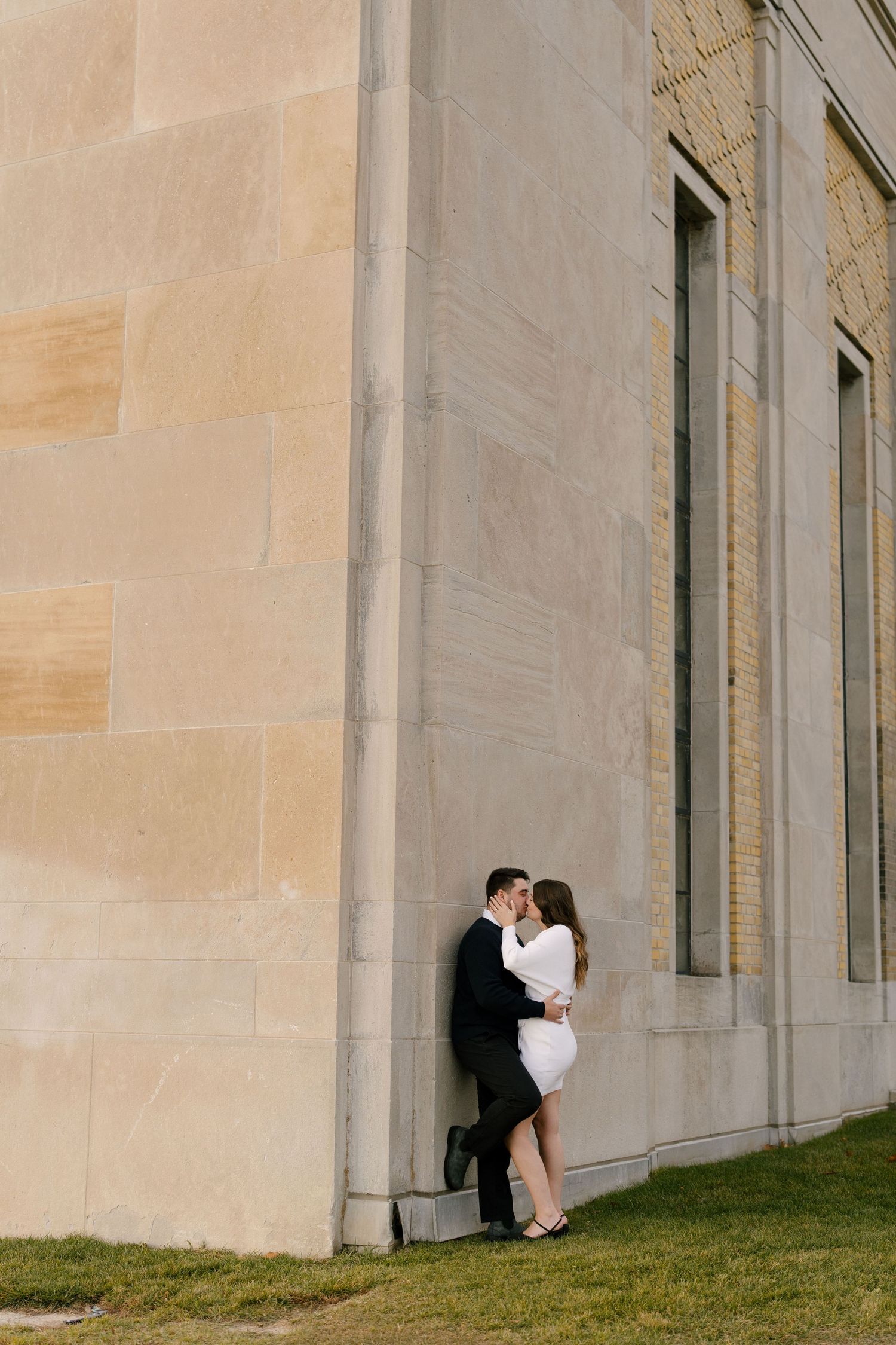 Romantic couple sharing a kiss while leaning against a stone building wall.