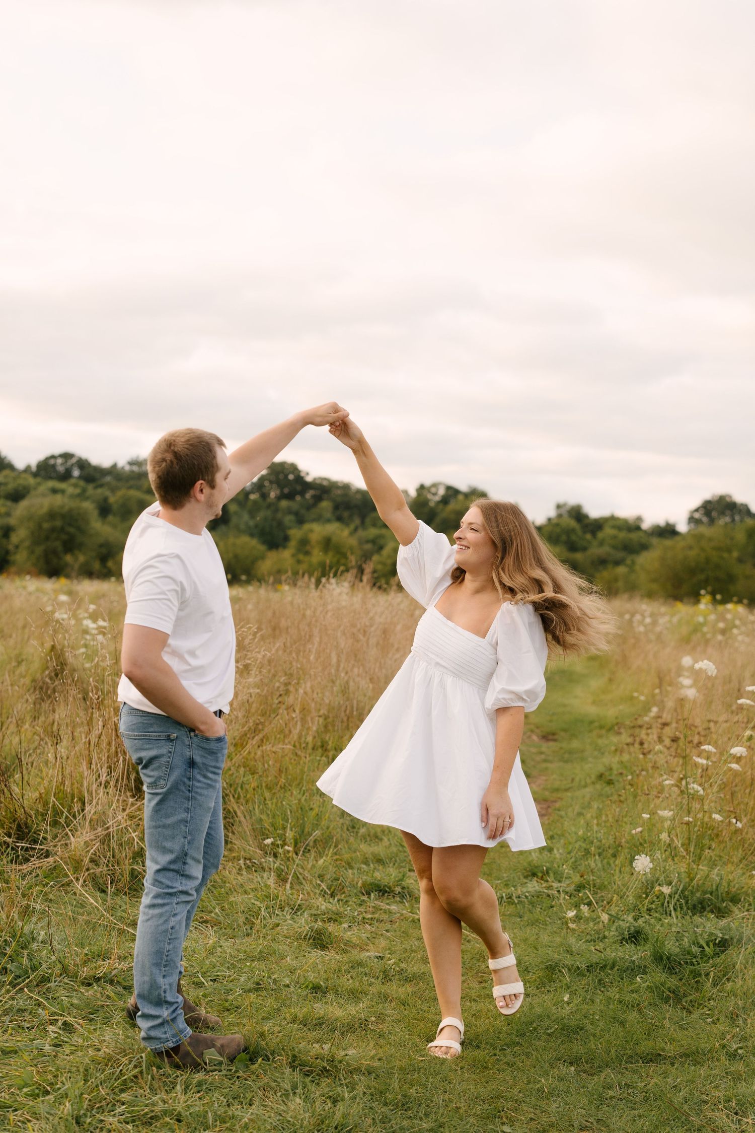 Couple dancing together in a wildflower meadow, woman twirling in a white dress.