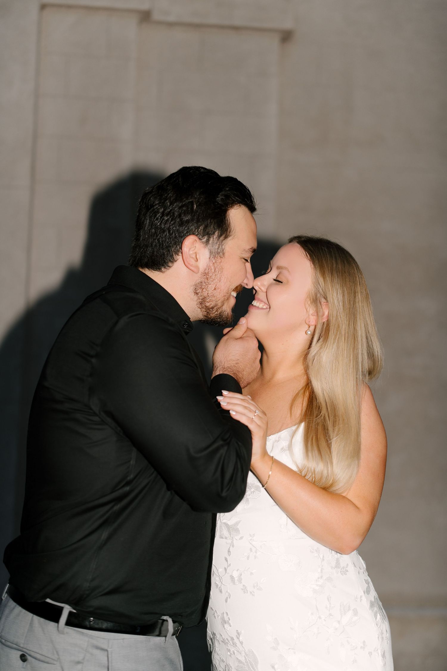 Romantic couple nearly kissing at night, woman in white lace dress laughing joyfully outdoors.